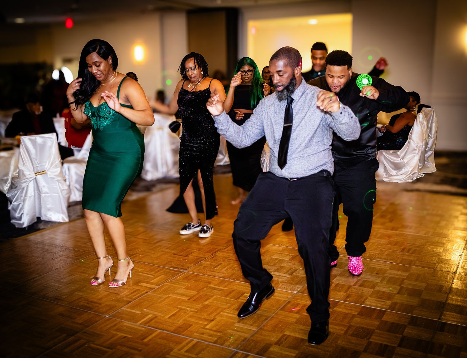 People dancing energetically at a formal event in a ballroom, wearing elegant attire including a green dress and suit.