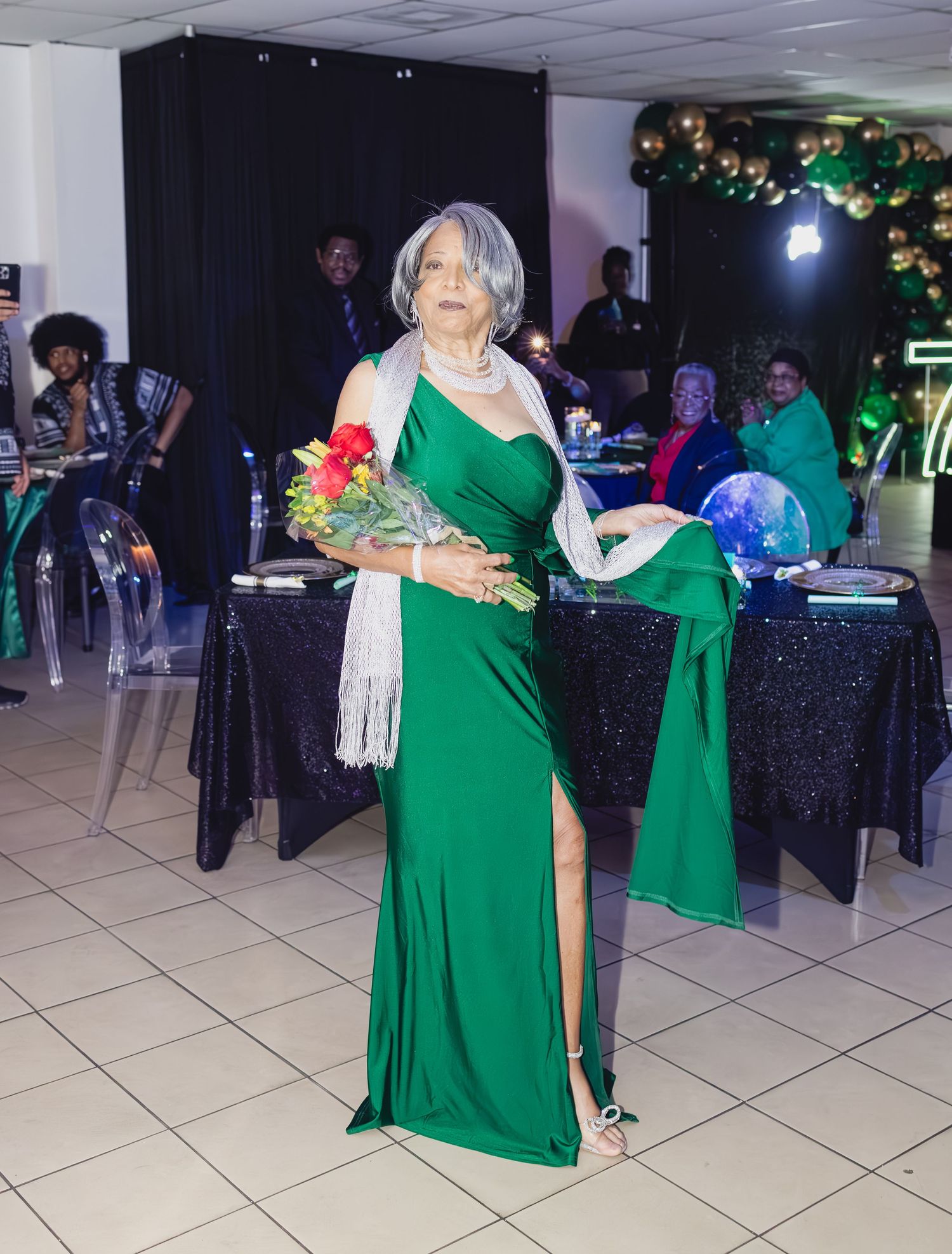 Someone wearing a stunning emerald green gown holds flowers at an elegant evening celebration.