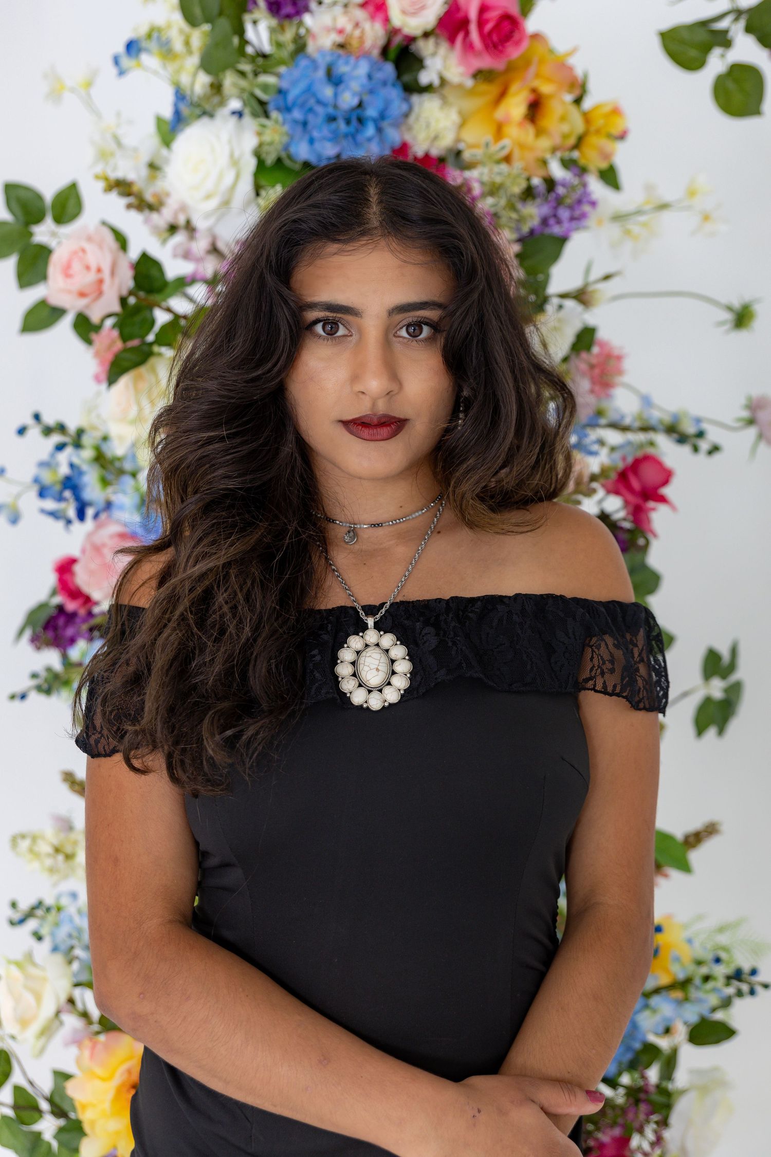 Portrait session featuring black off-shoulder dress against wall of colorful spring flowers.