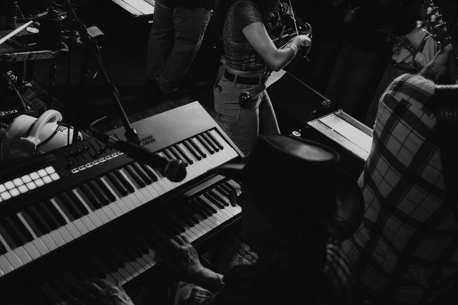 Black and white overhead view of musicians playing keyboards and synthesizers at a live jazz band performance.