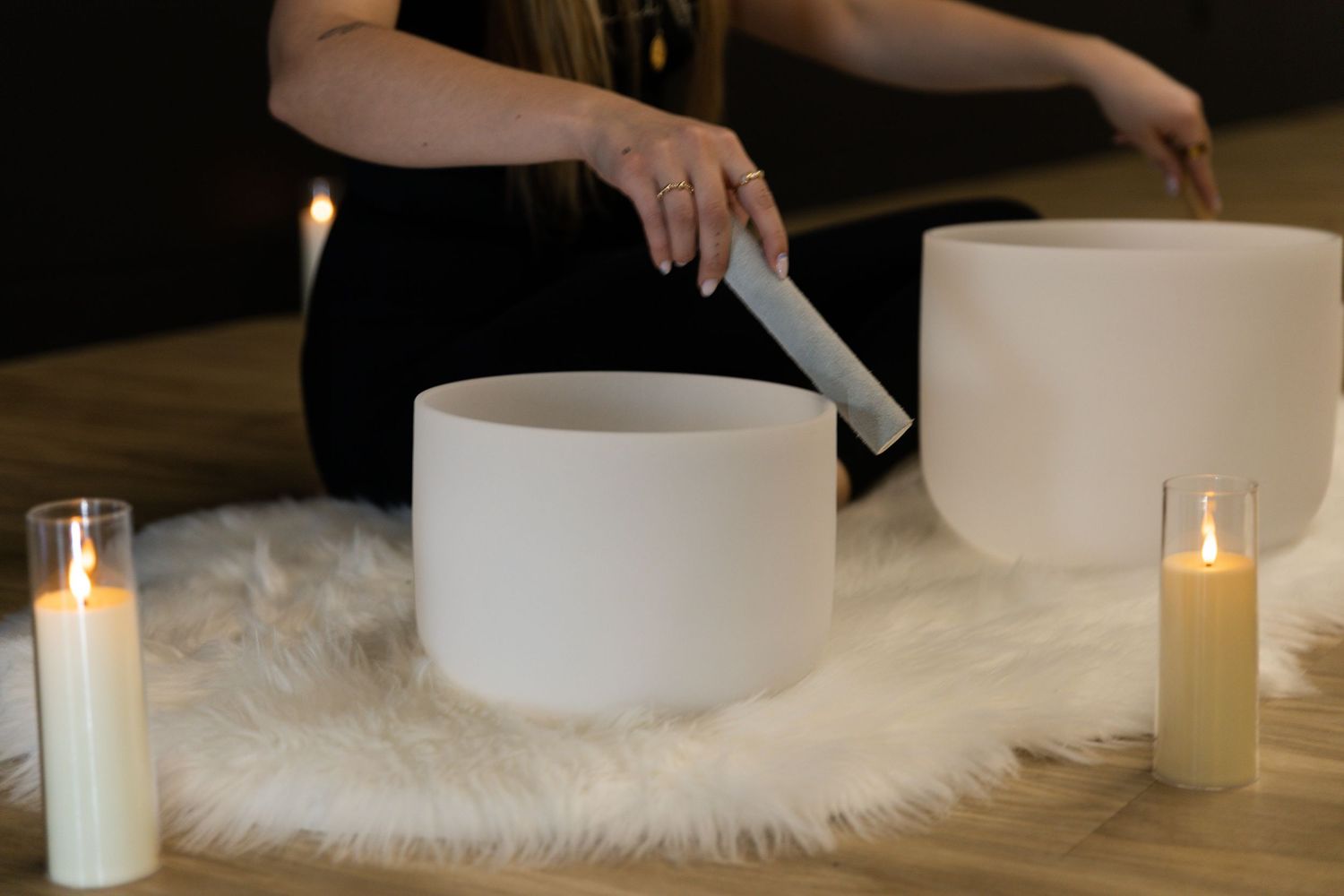 White candles arranged on a furry white surface with hands lighting them.