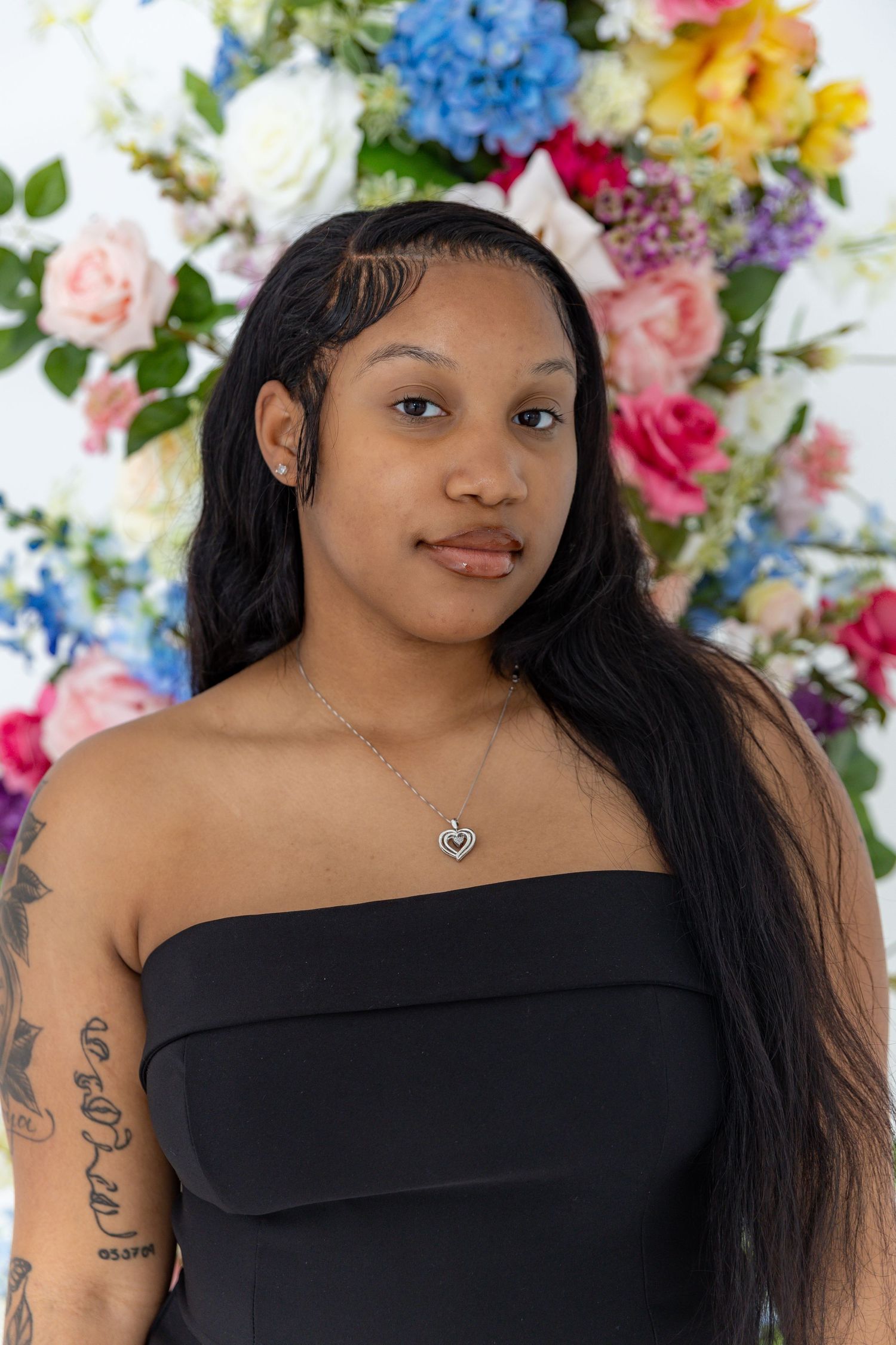 Off-shoulder black dress portrait with colorful floral backdrop featuring hydrangeas and roses.