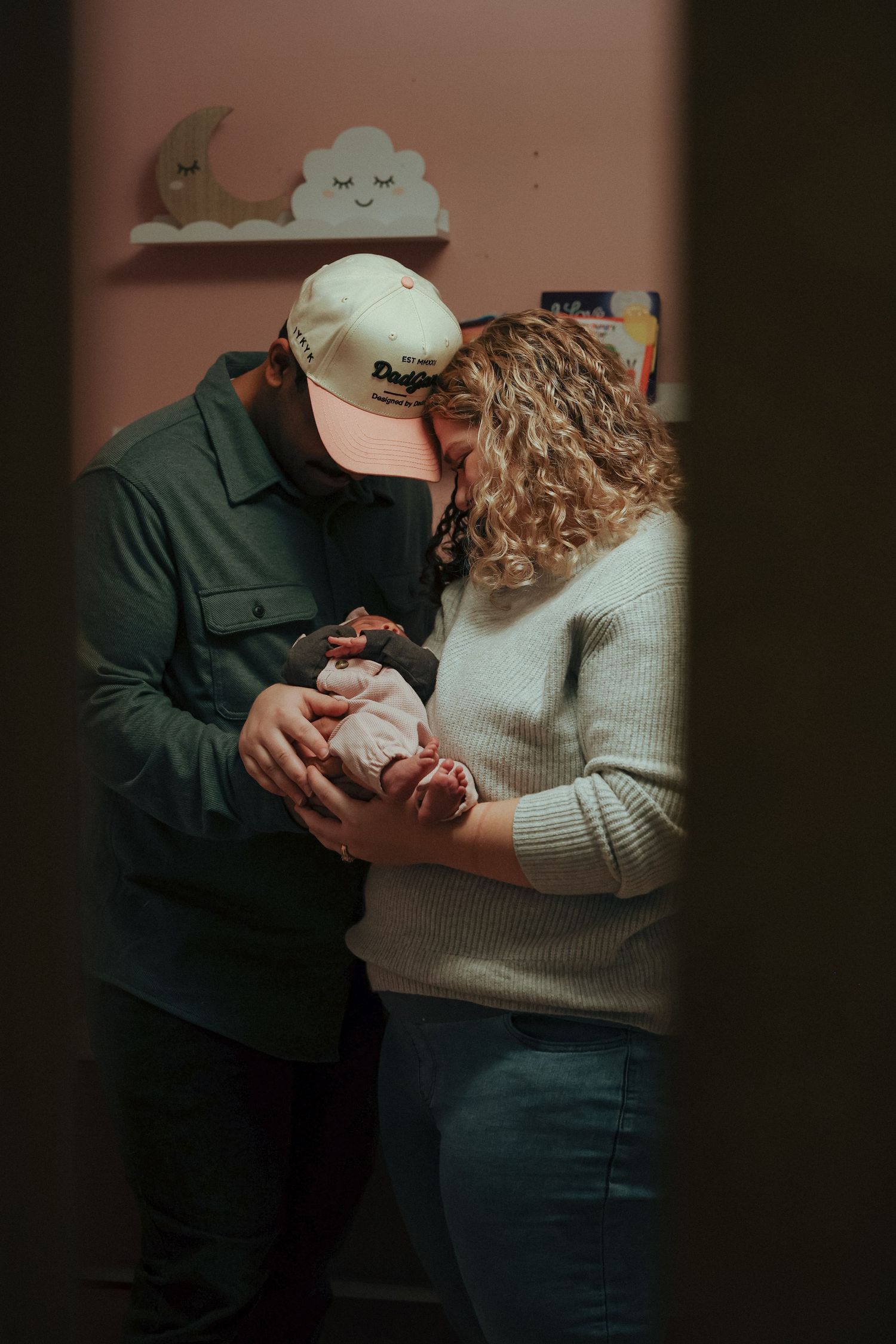 mom and dad looking down at newborn at home in nursery