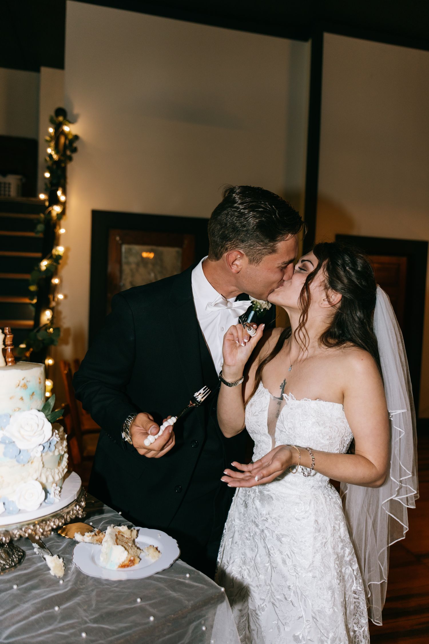 Bride and groom share a kiss while cutting their white wedding cake at their reception.