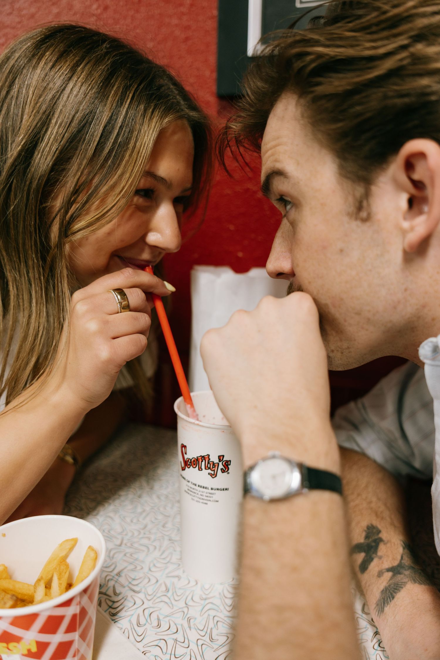 Couple sharing a milkshake with fries at Scotty's diner, smiling intimately at each other.