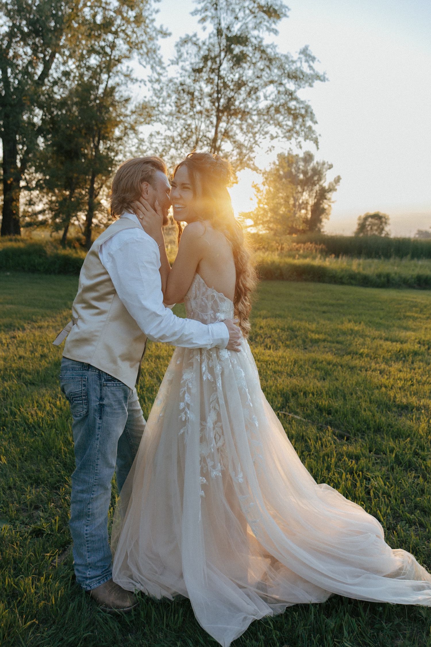Couple sharing intimate moment during sunset wedding photoshoot in pastoral setting.