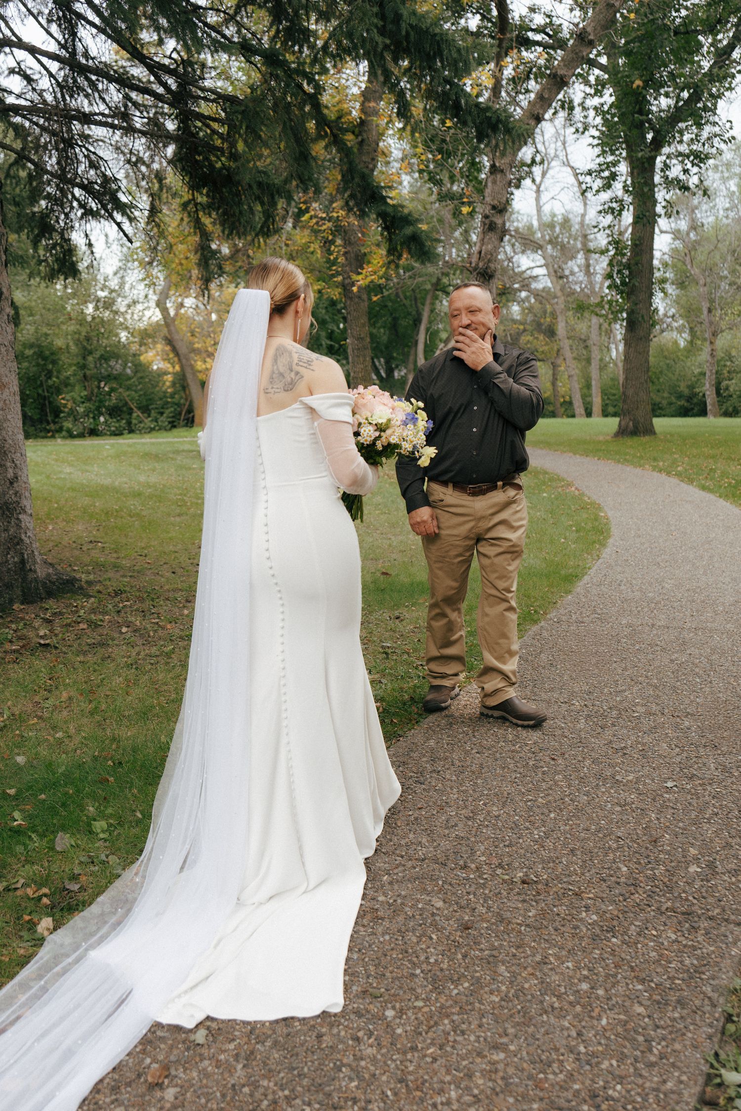 Wedding dress train flowing on a gravel path surrounded by autumn trees.