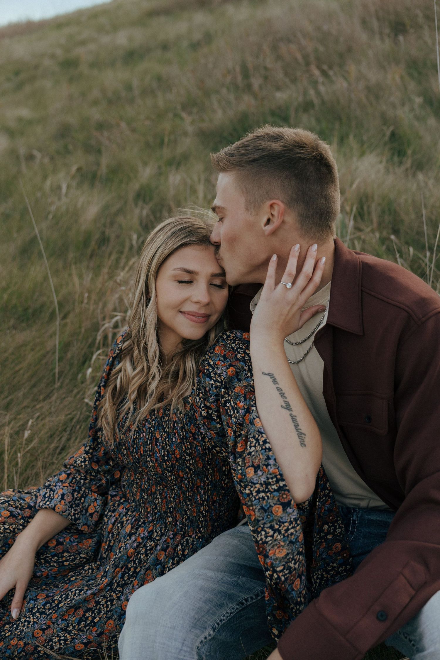 Romantic couple portrait with woman in floral dress and man in brown jacket outdoors.