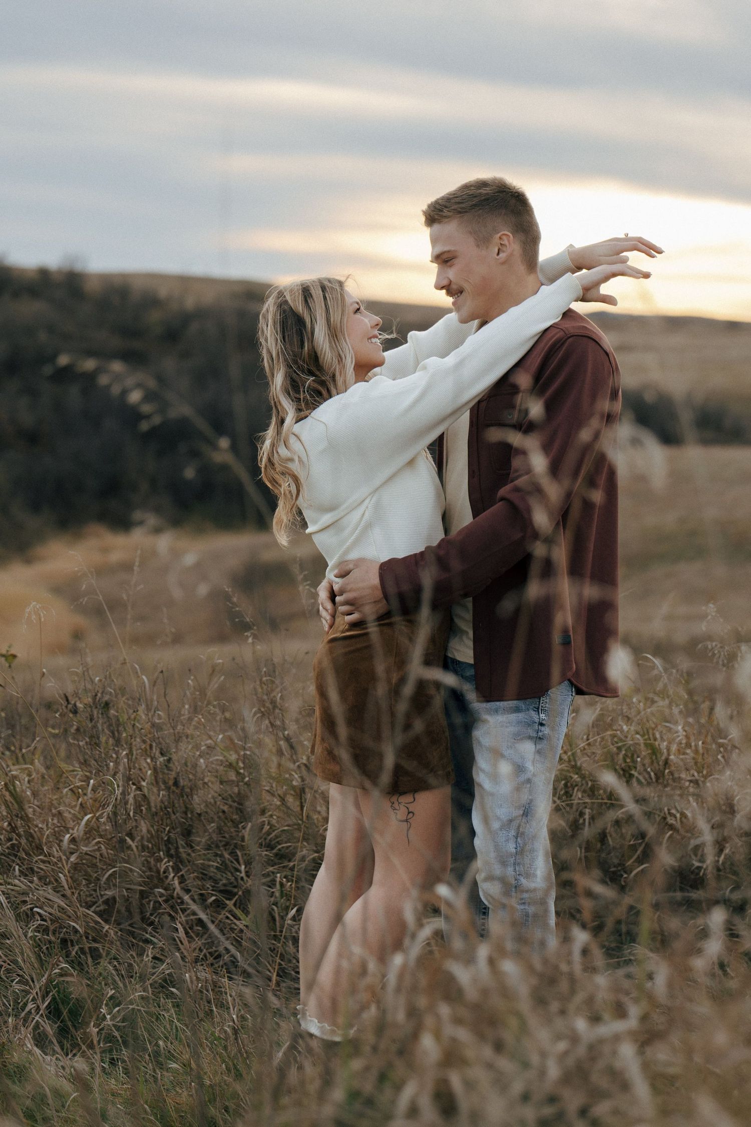 Couple embracing in a field of tall grass during sunset.