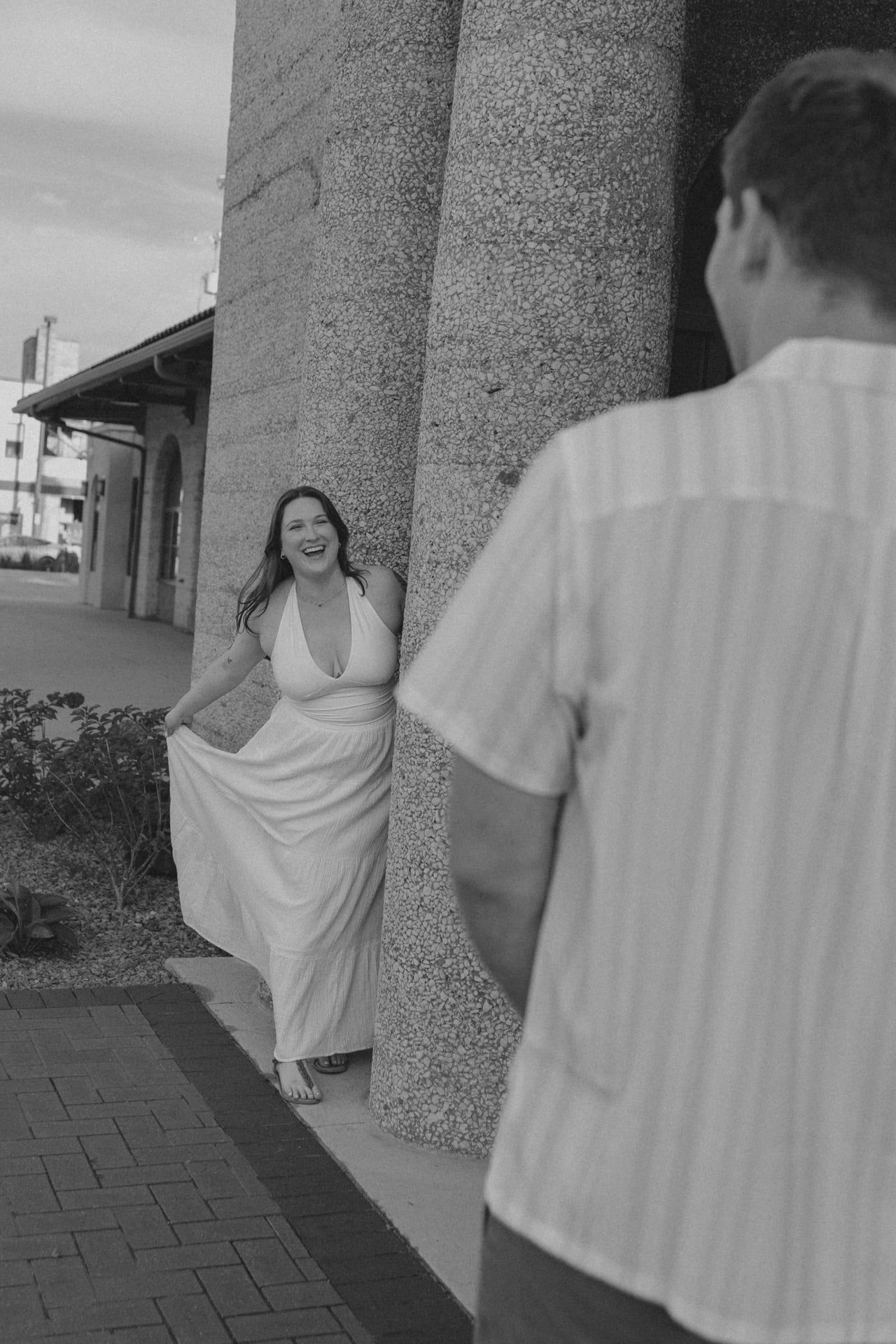 A playful couple poses between columns in black and white, with a flowing white dress creating movement.