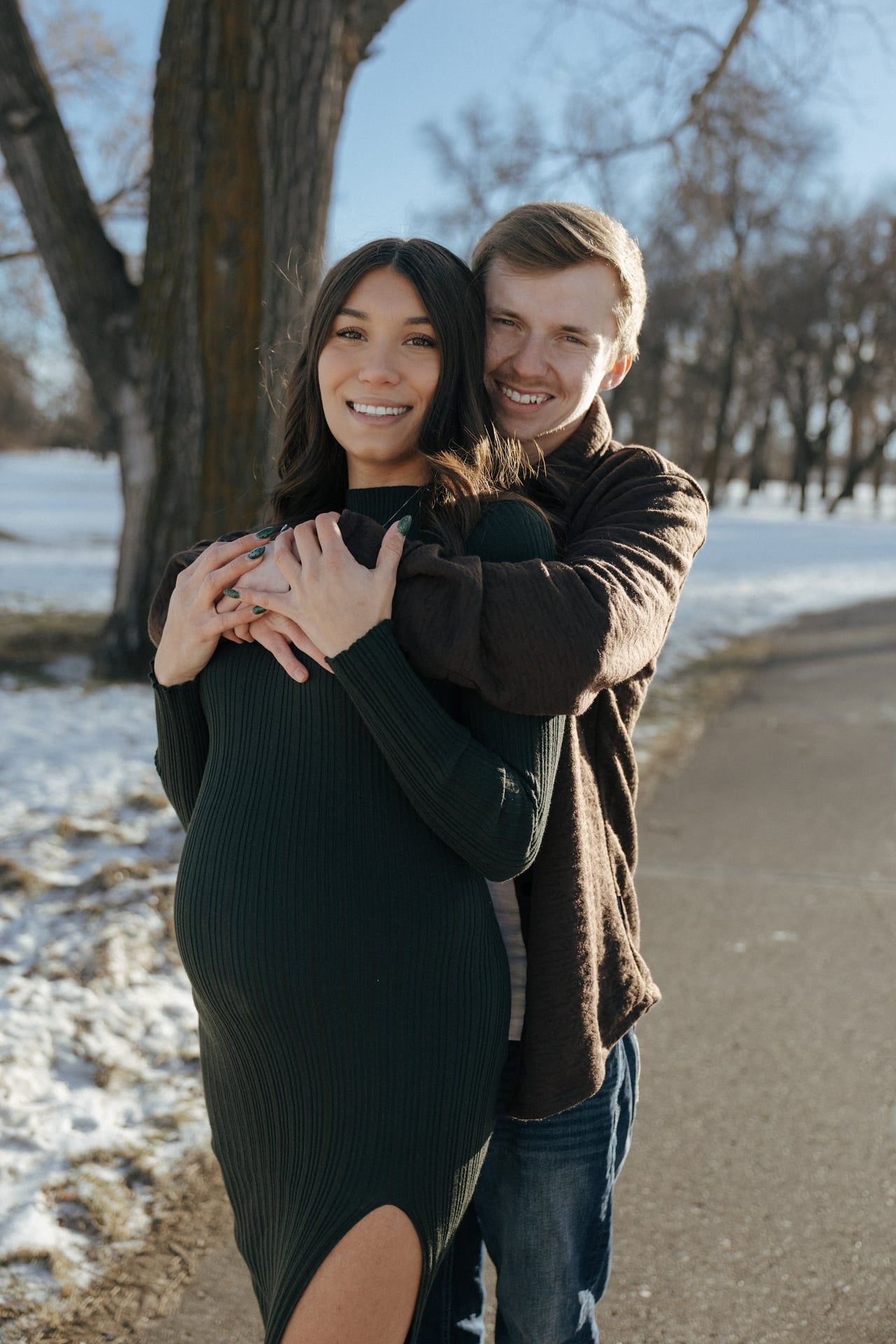 Couple cuddling in snowy park for maternity session