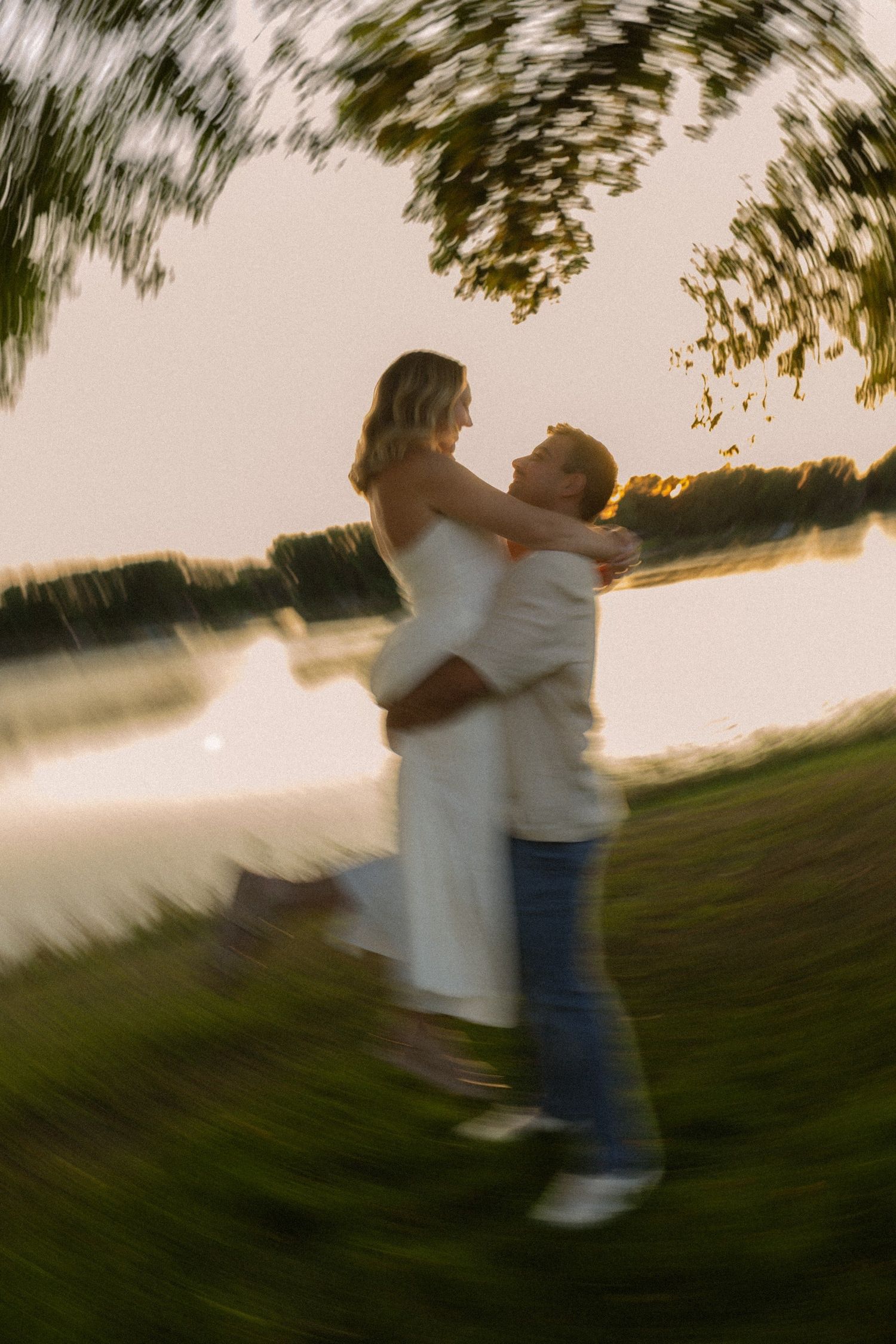 Motion-blurred artistic photo of a couple embracing by a lake at sunset.
