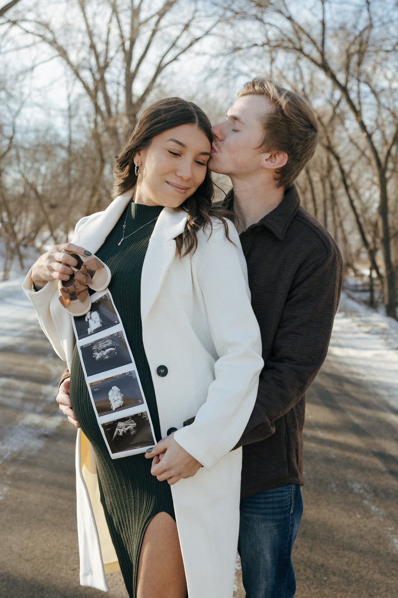 man kissing girls forehead in snowy trees in Bismarck with ultrasound photos