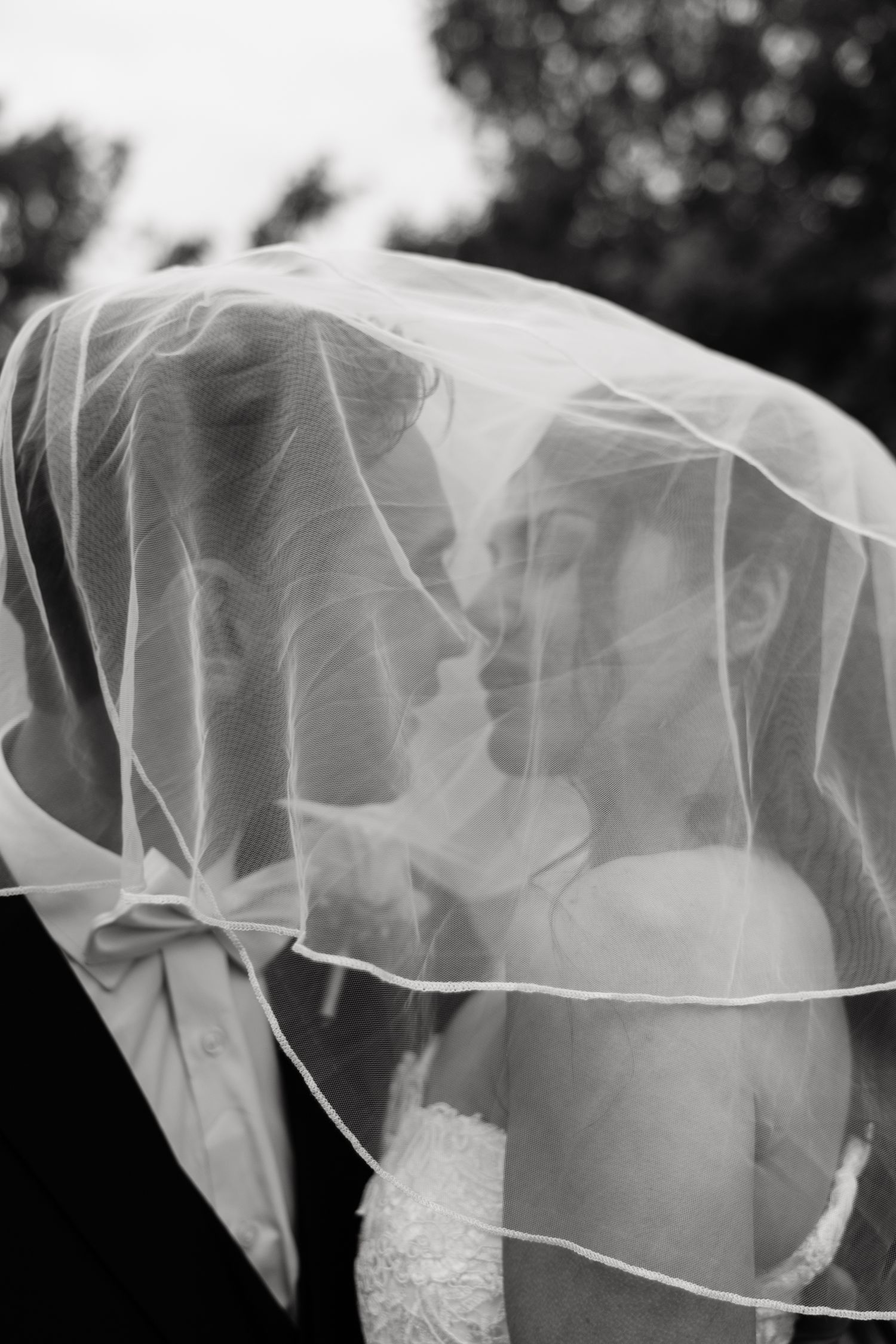 Romantic black and white photo of a bride and groom sharing an intimate moment under a flowing wedding veil.