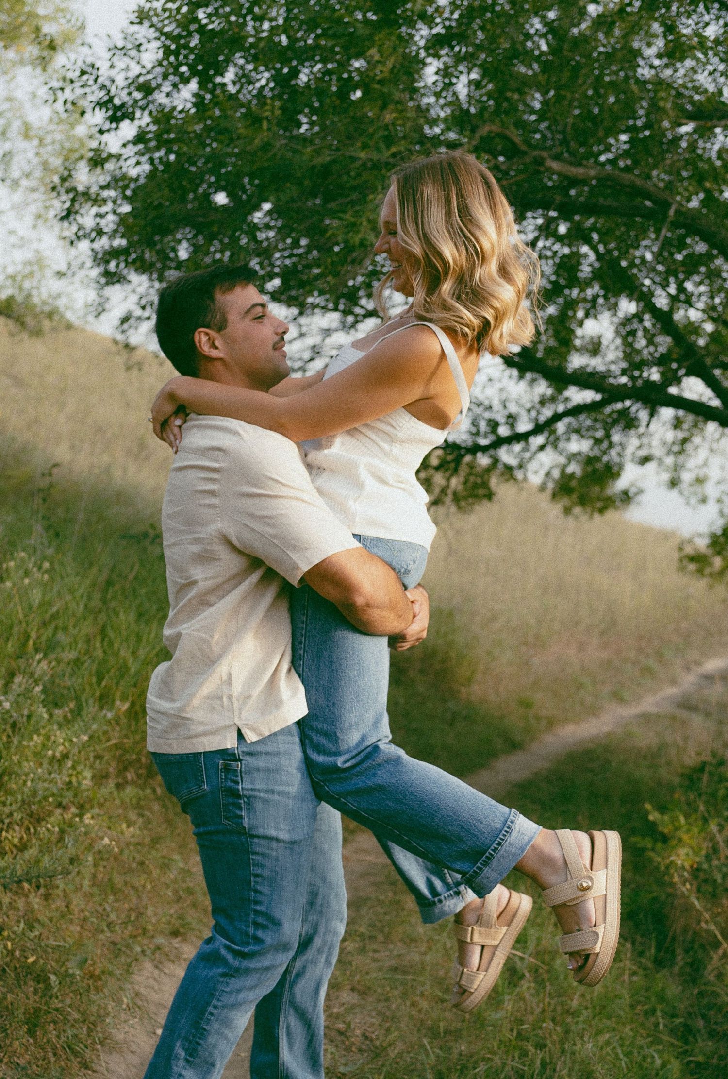A playful scene of two people embracing in a natural outdoor setting with trees.