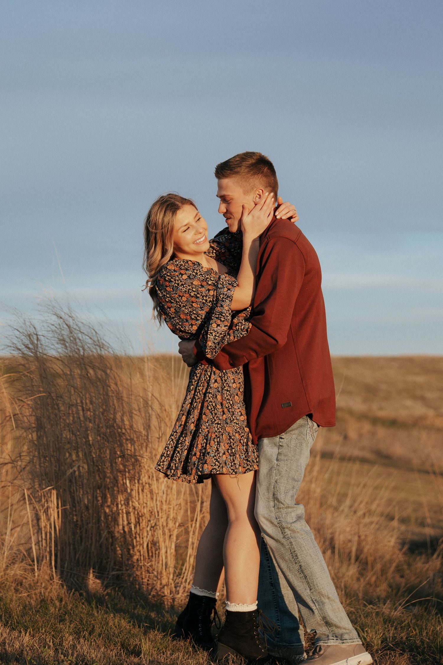 Couple laughing and embracing in a field during golden hour.