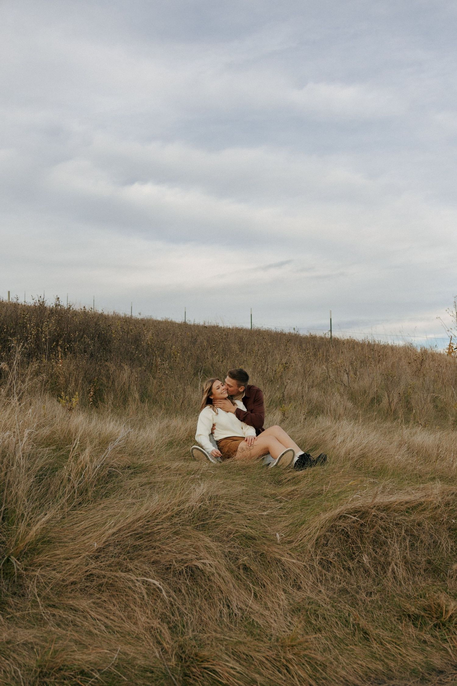 Someone relaxes in tall grass on a hillside under cloudy skies.