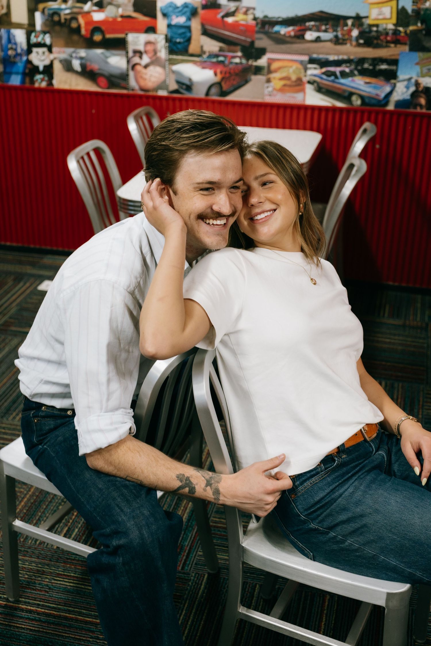A happy couple cuddles and smiles together while sitting in chairs inside a retro diner.