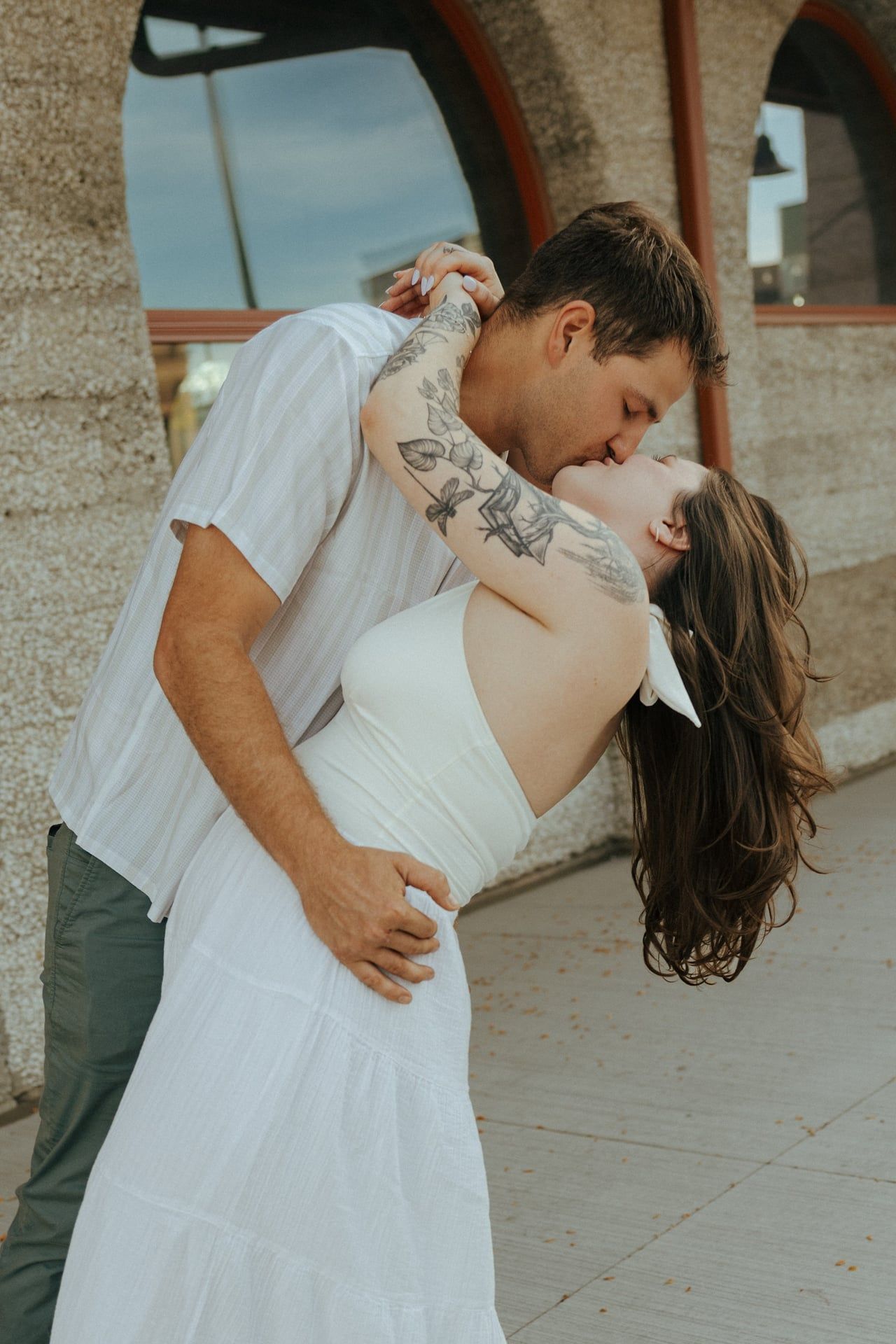 A romantic dip kiss captured in warm sunlight against a stone building exterior.