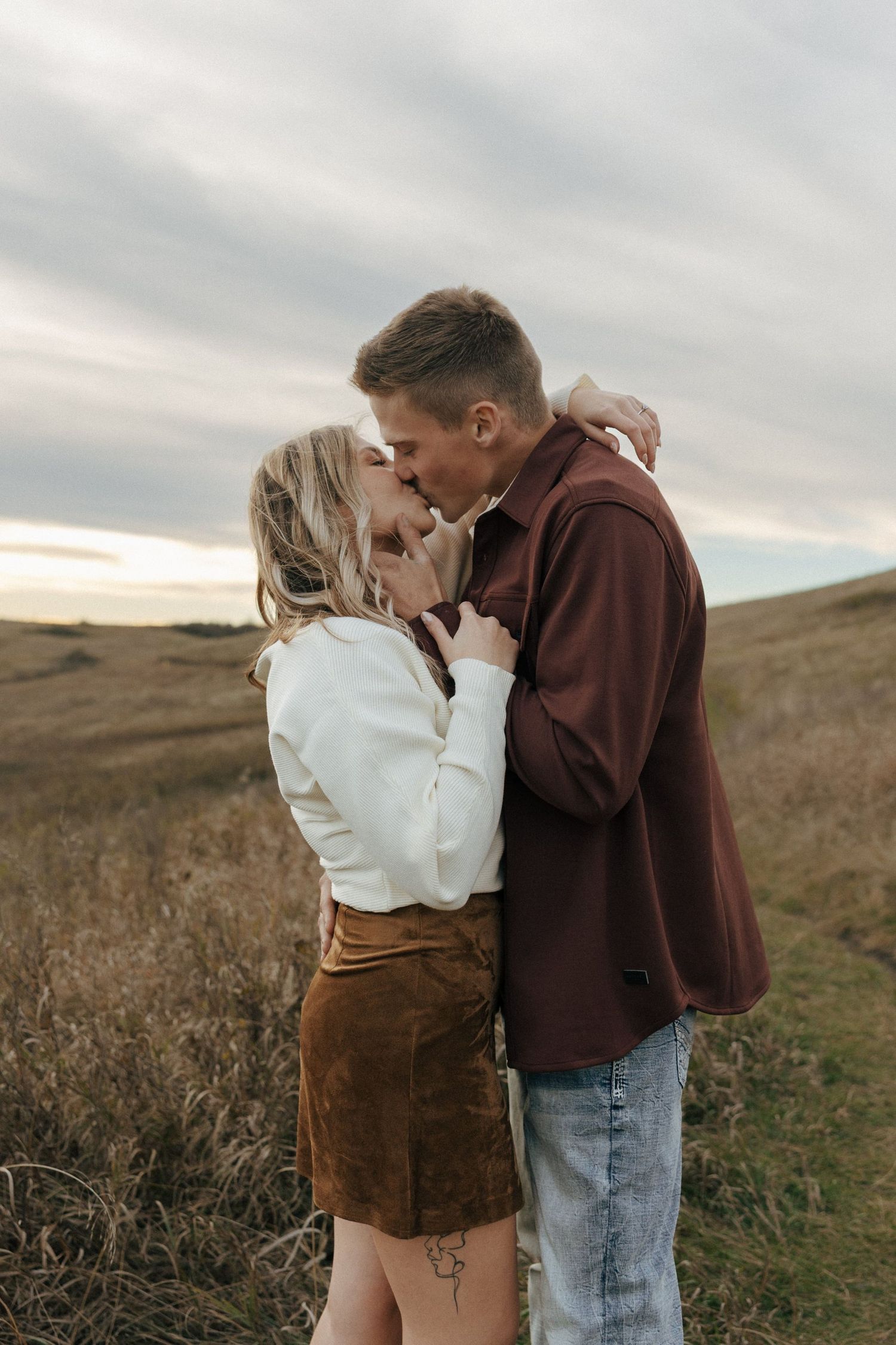 Couple in casual autumn wear sharing a tender moment in a grassy field at sunset.