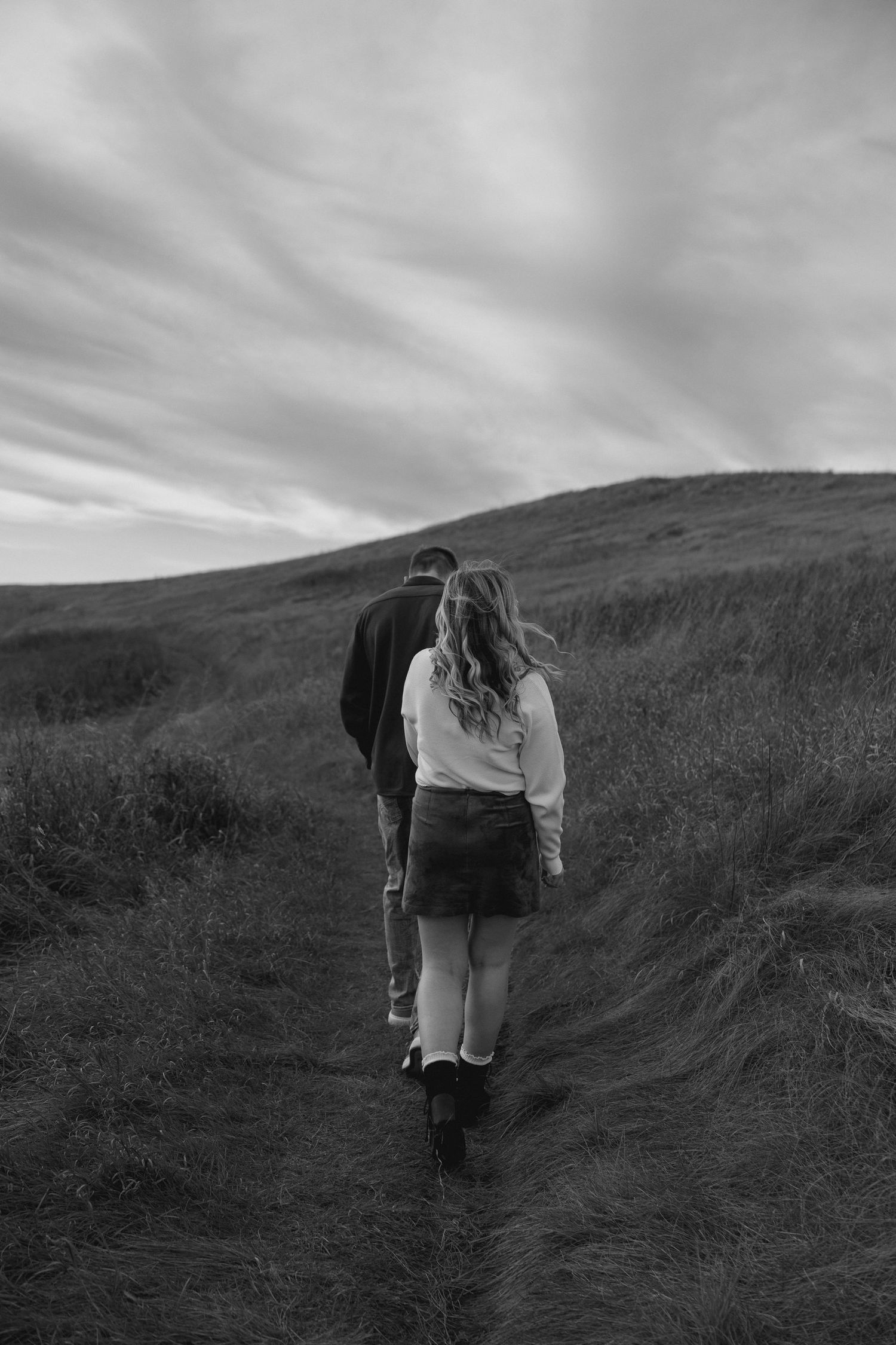 Black and white photo of two people walking uphill on nature trail.