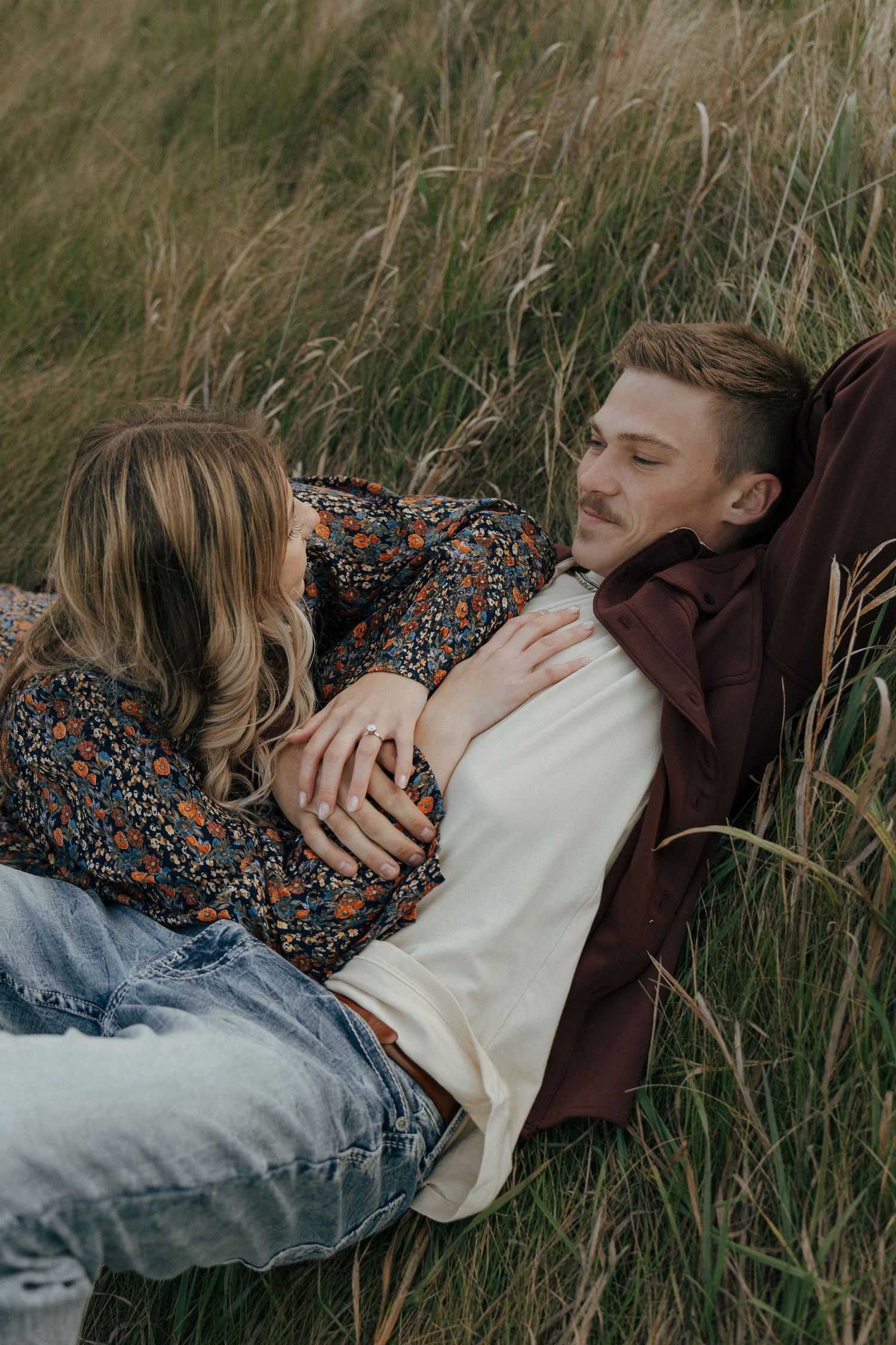 Couple lying in tall grass during romantic outdoor photography session.
