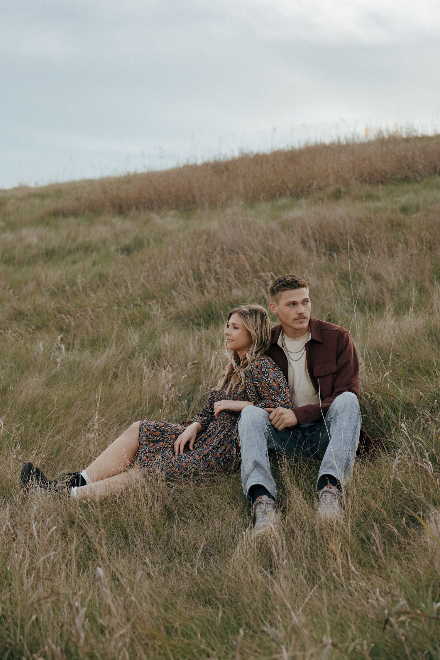 Couple relaxing together in tall grass on a hillside during sunset.