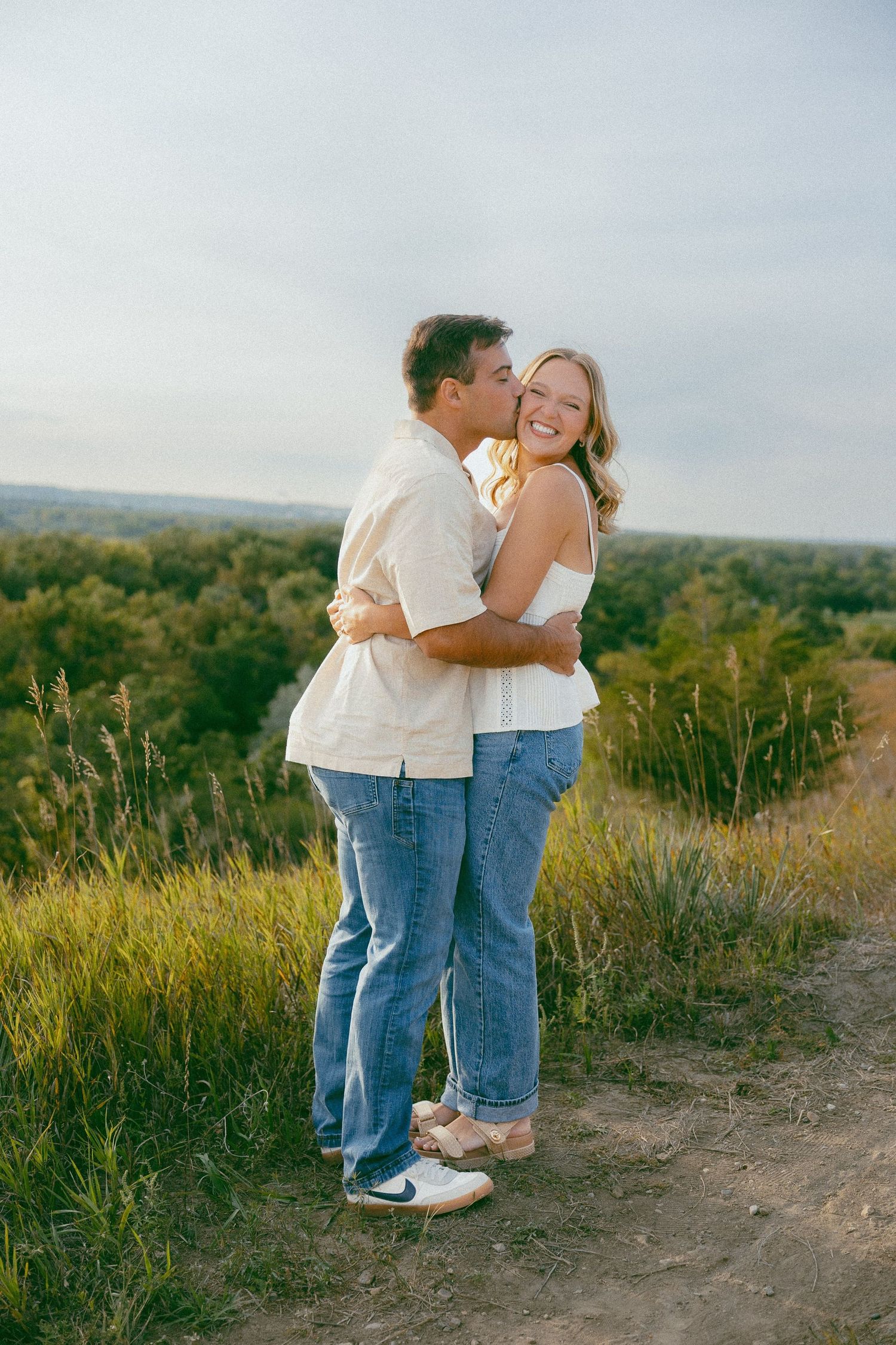 A couple shares a romantic moment together on a scenic trail overlooking rolling hills.