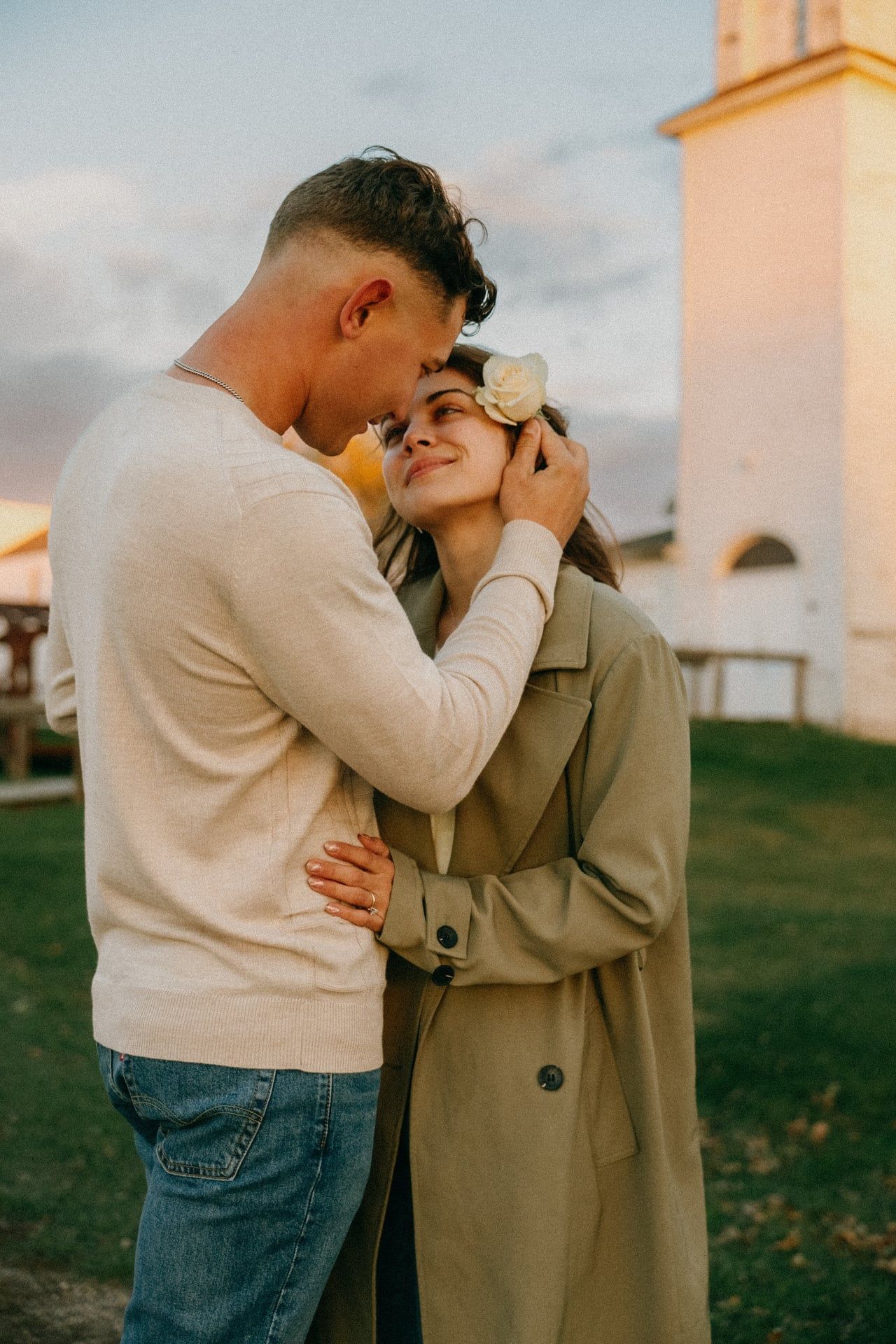 A couple embraces tenderly outdoors against a sunset sky and white church backdrop for an engagement session in Bismarck at Buckstop.