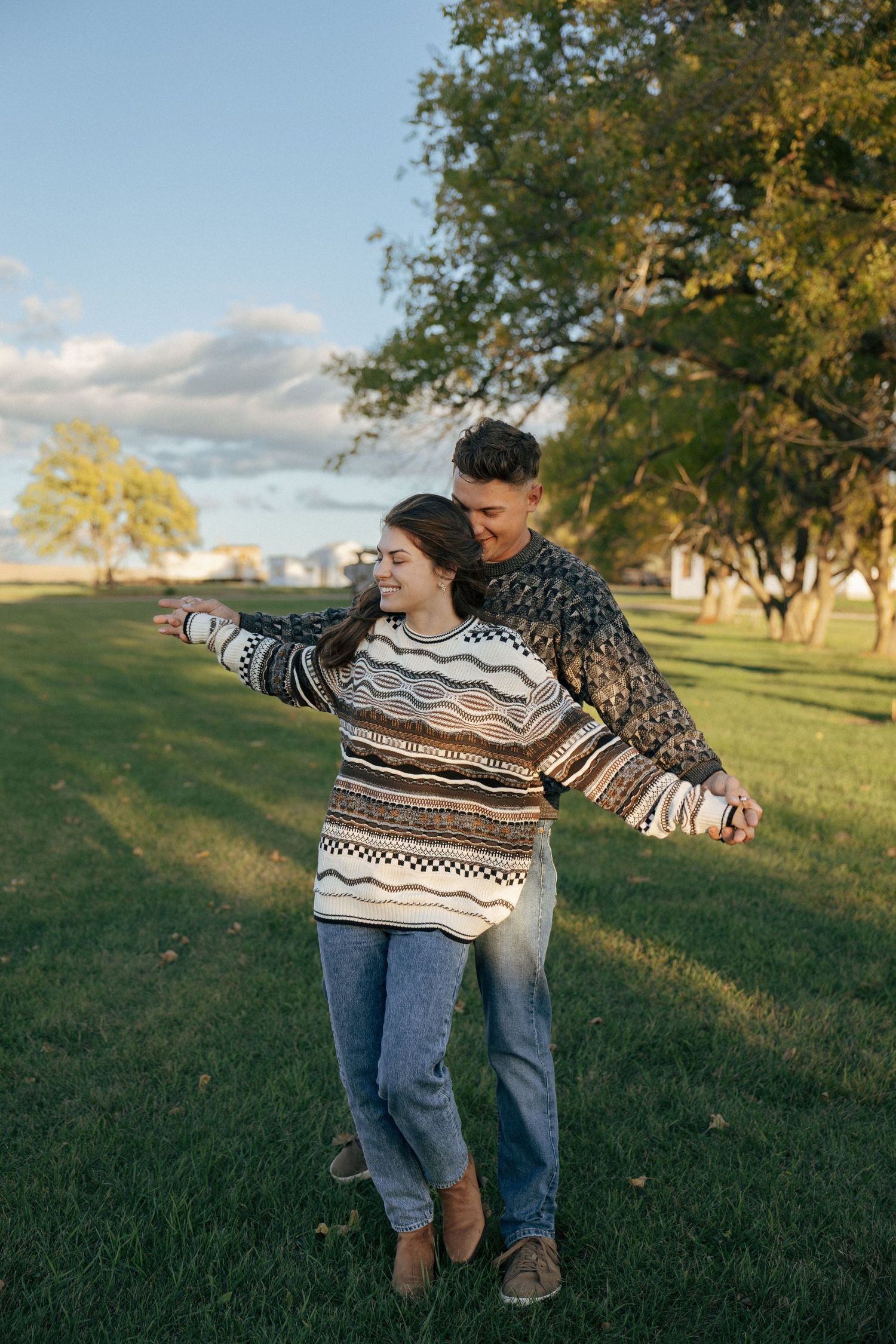 A couple wearing matching sweaters shares a playful moment in a sunny park setting.