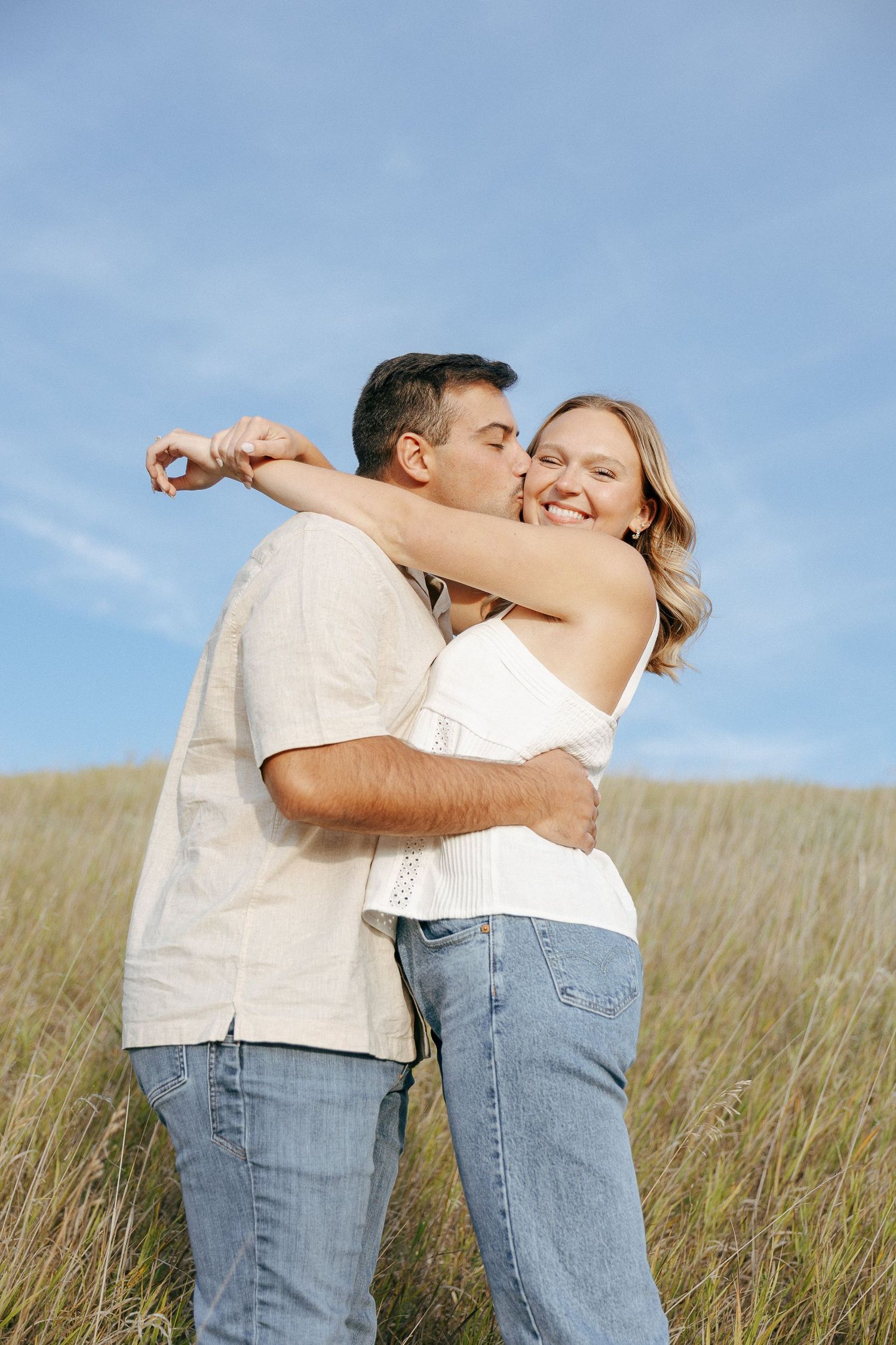 An intimate moment between two people standing in a field of tall grass under blue skies.