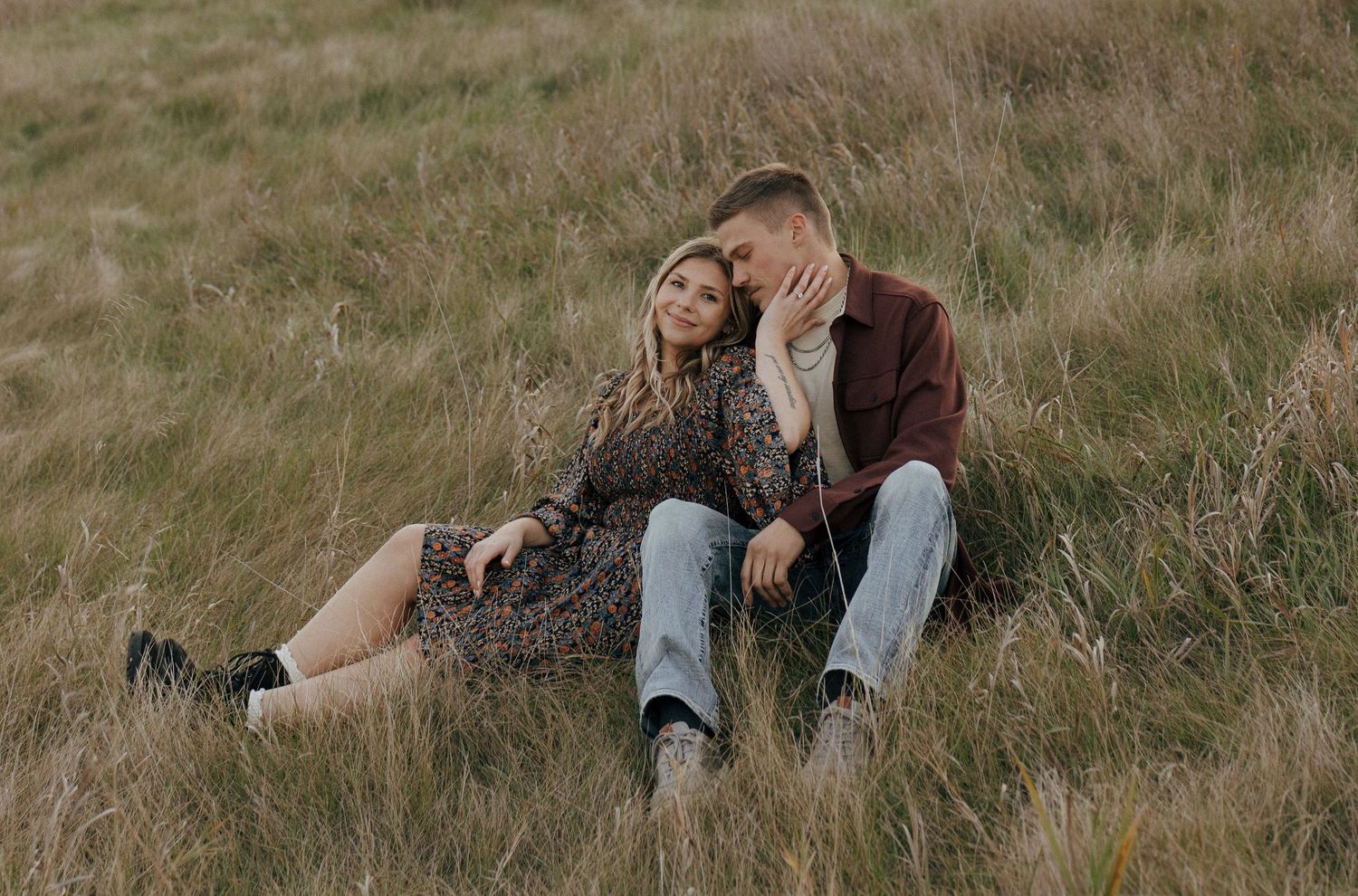 Intimate moment captured of couple resting on grass slope in natural setting.