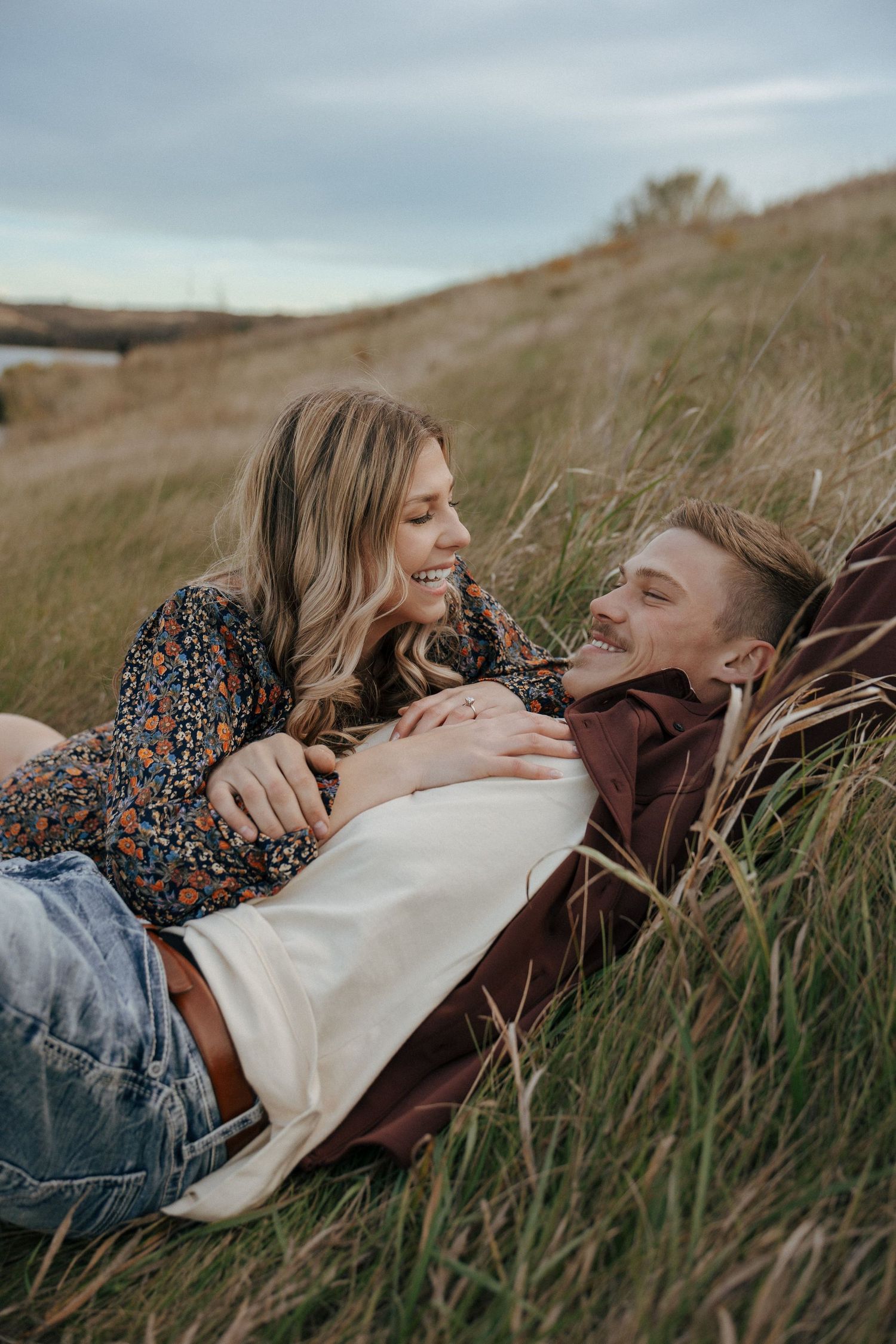 Romantic couple relaxing in tall grass field against cloudy sky.