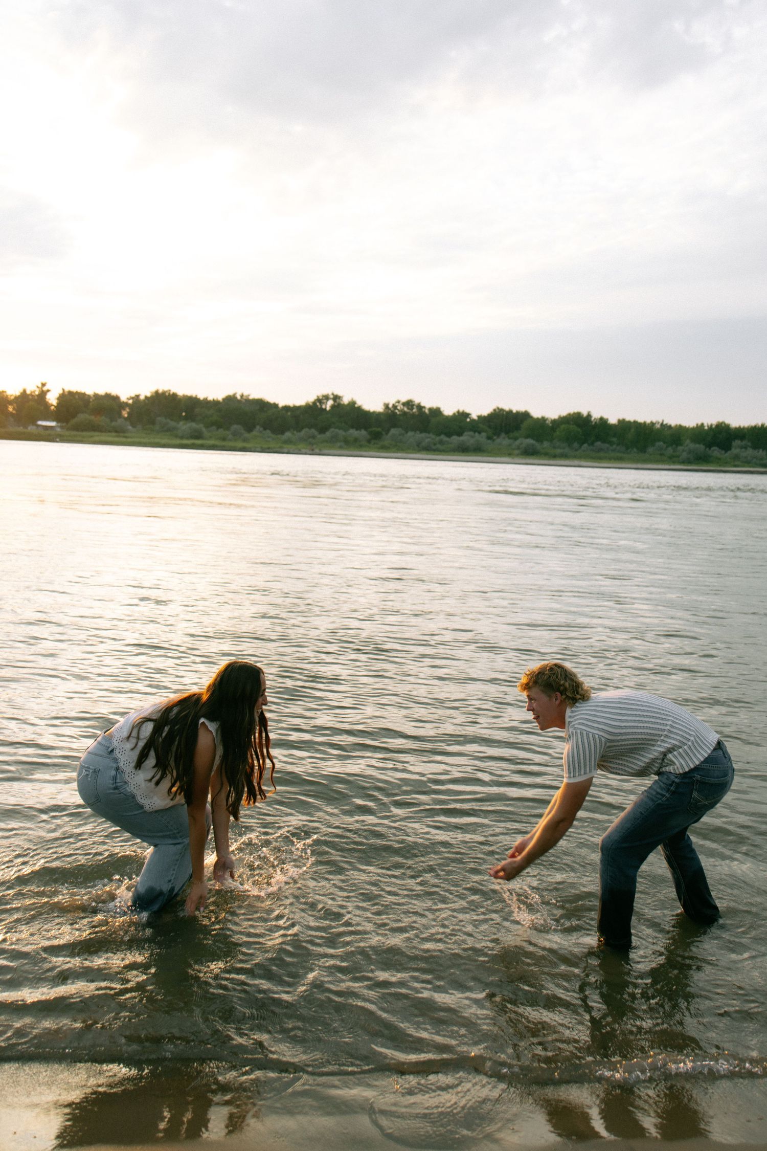 Two people splashing in a shallow river at sunset, enjoying a playful moment in the water.