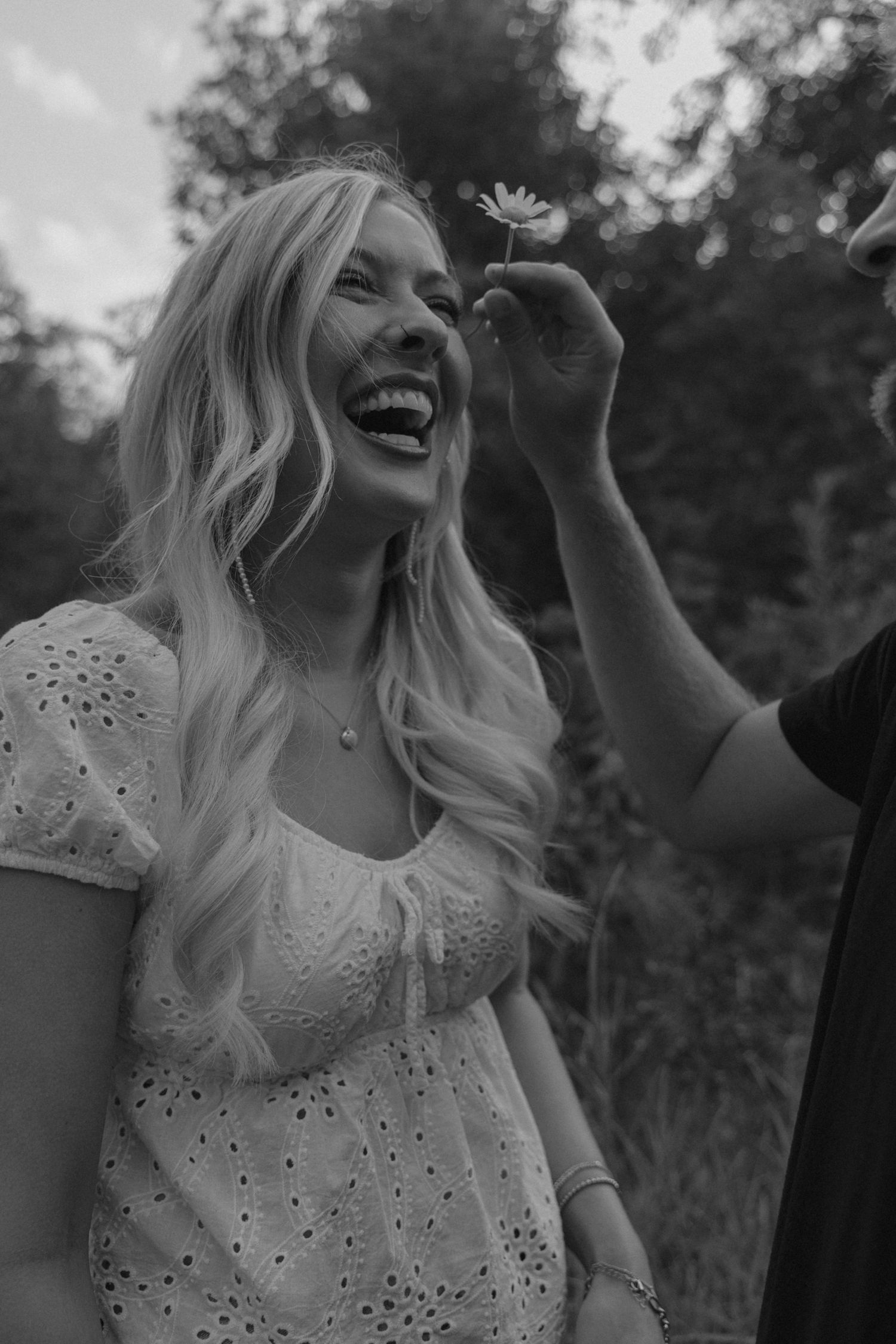 Guy putting flower in fiancee's hair making her laugh during engagement session in Spearfish South Dakota