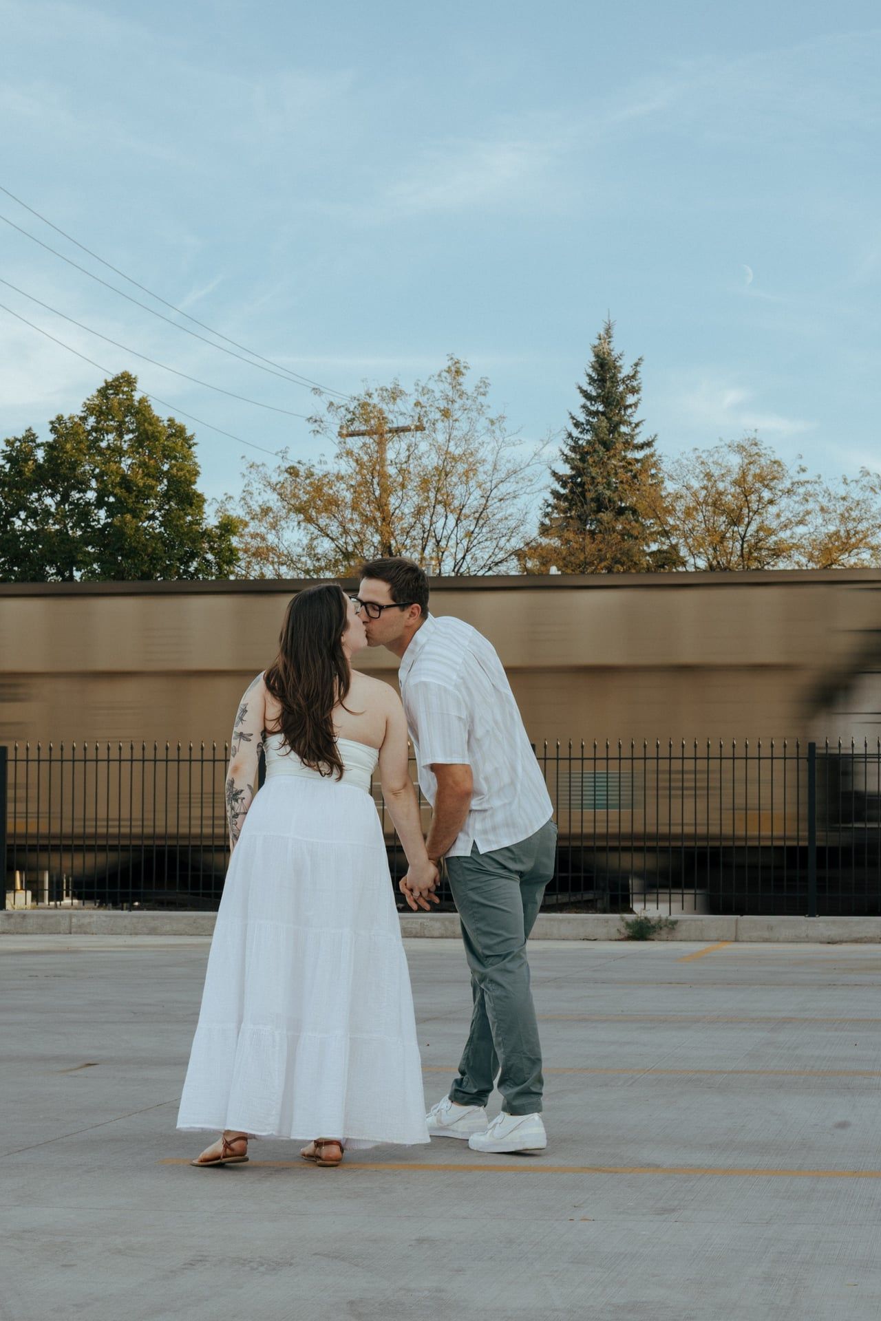 A couple shares an intimate moment outdoors against a blue sky and urban backdrop.