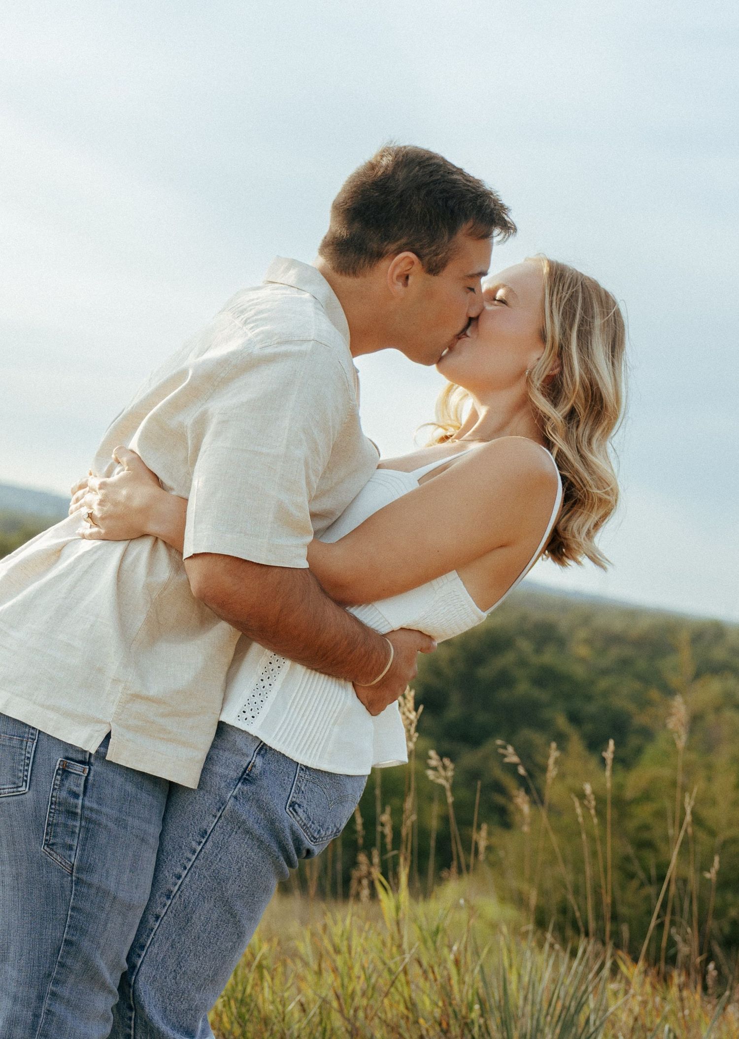 Two people in casual wear share an affectionate embrace on a hilltop trail.