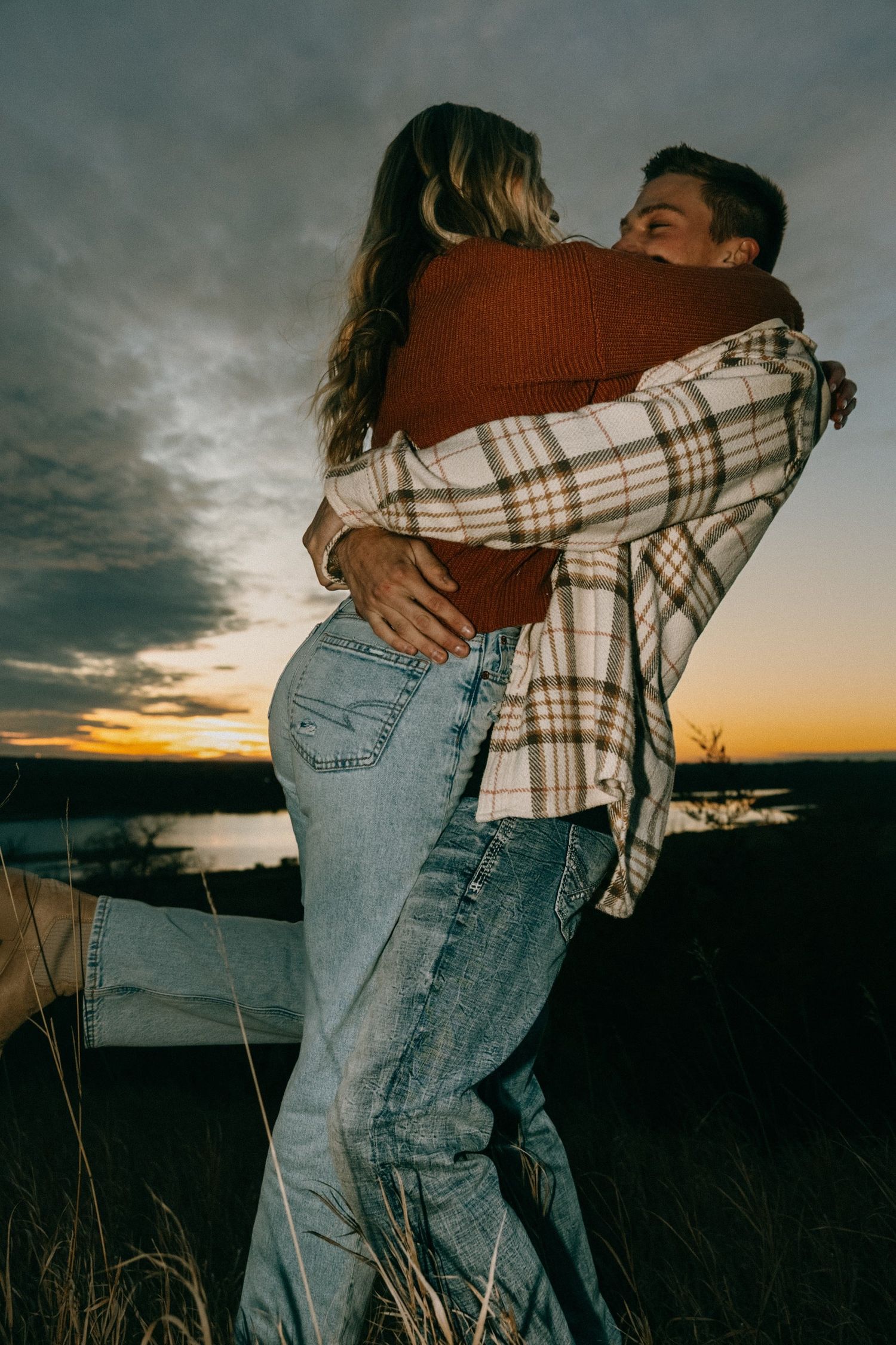 Intimate sunset portrait of couple in casual wear hugging against dramatic sky.