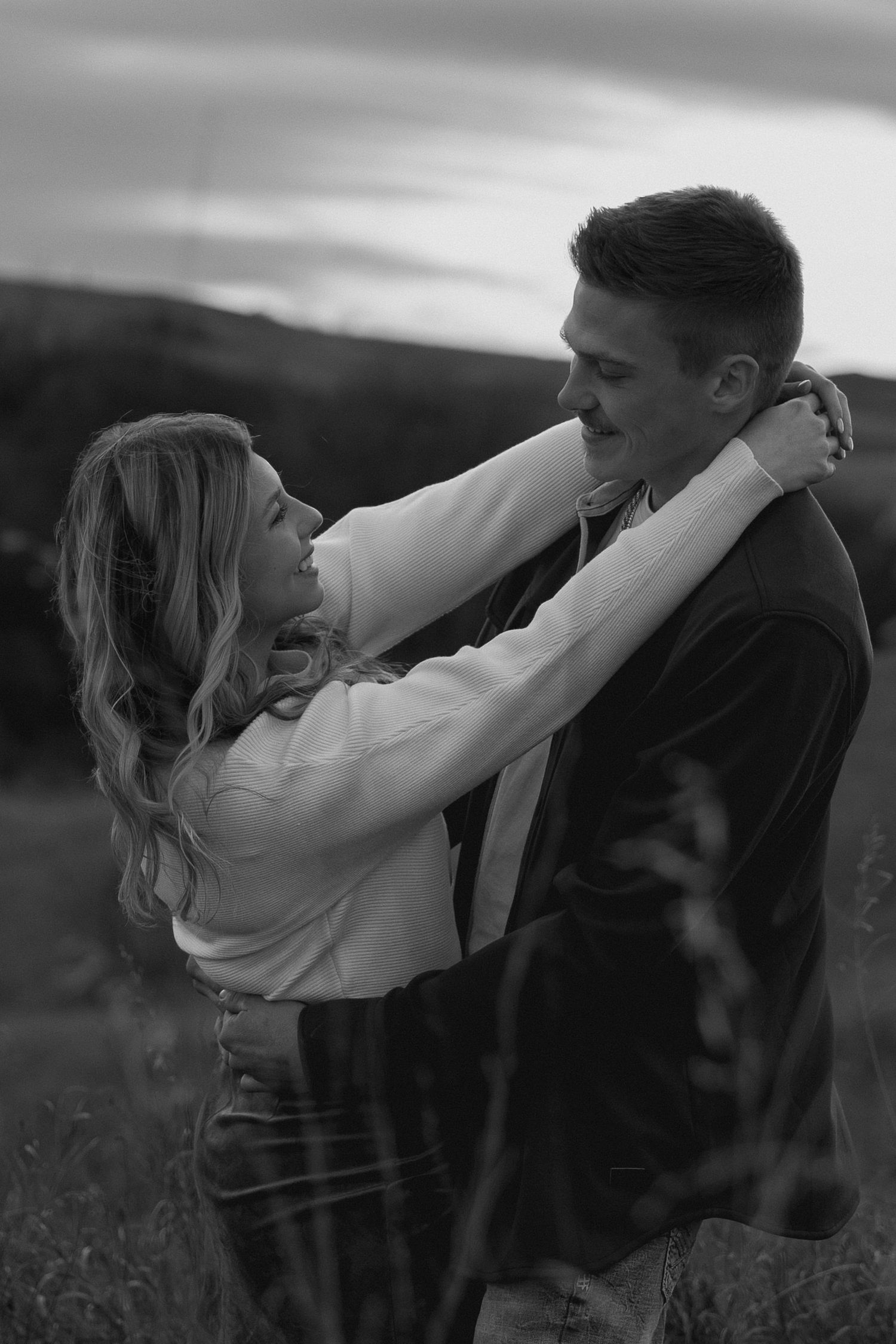 Black and white photo of a couple sharing an intimate moment in a field.