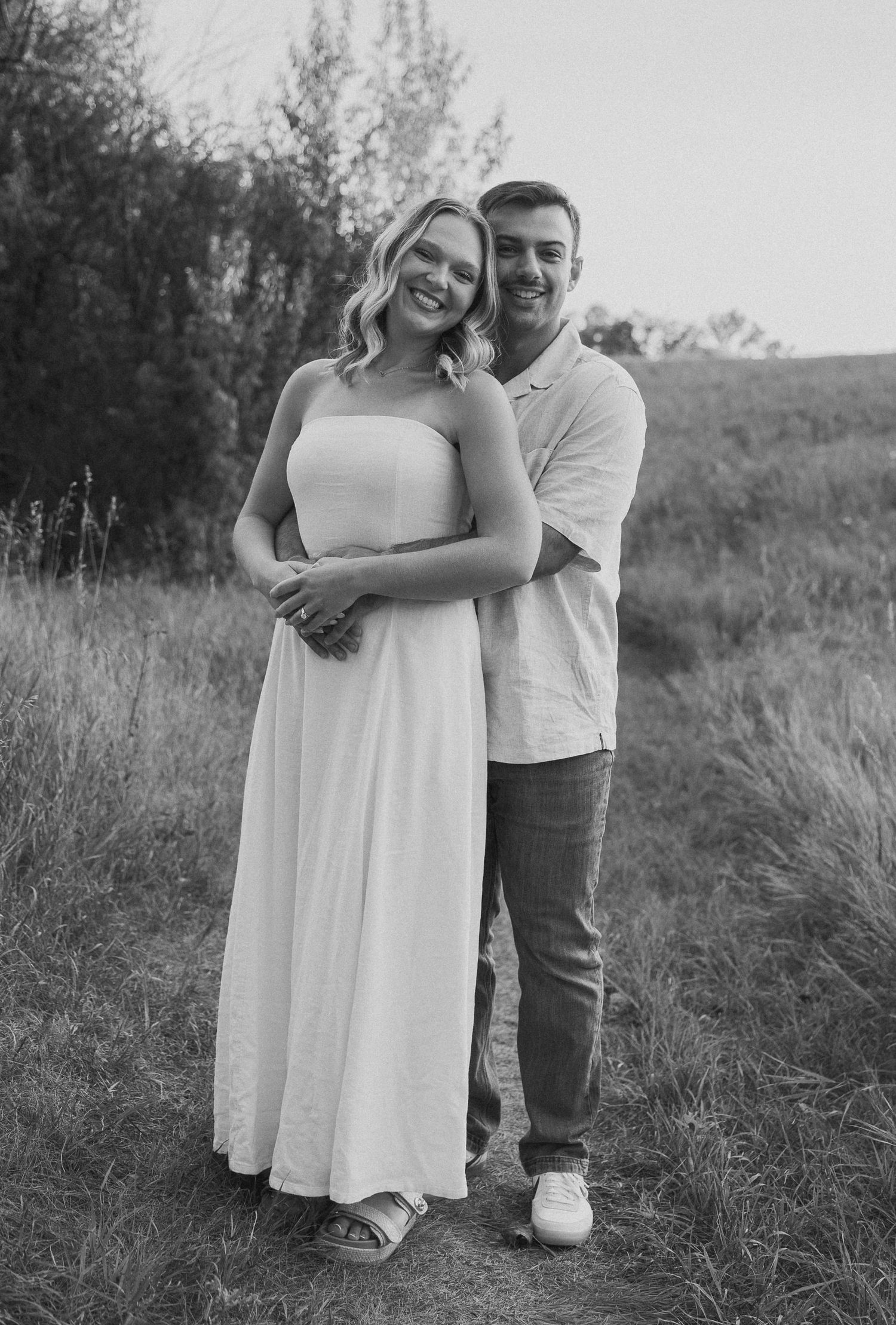A black and white portrait of a couple embracing on a hillside path.