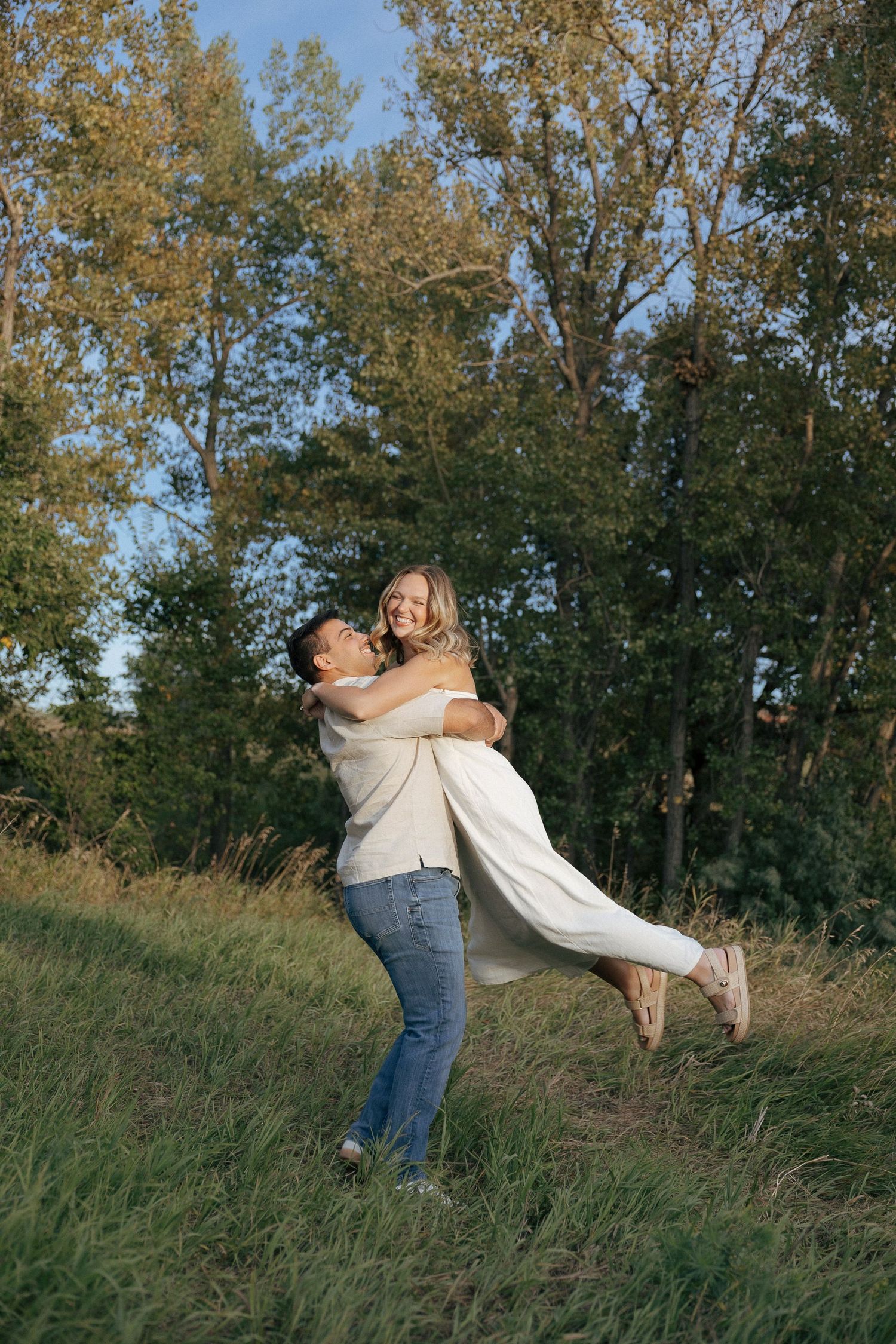 A couple dances and spins playfully on a grassy hillside during golden hour.