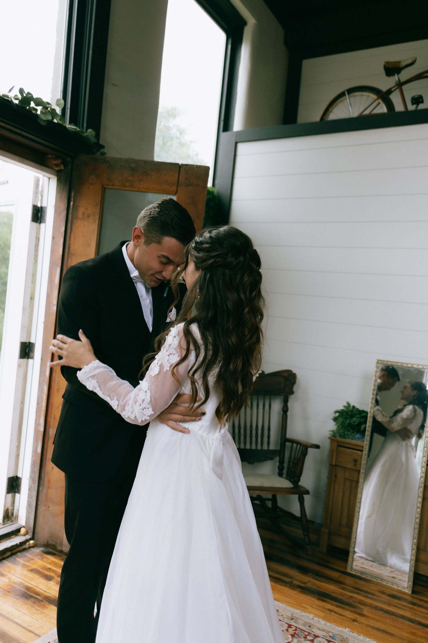 A bride and groom share an intimate first look moment, embracing indoors with rustic decor.