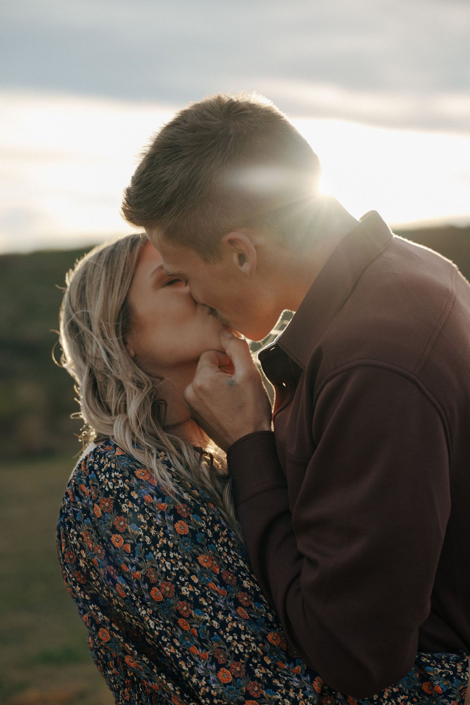 Intimate romantic moment captured between two people during golden hour on a hillside.