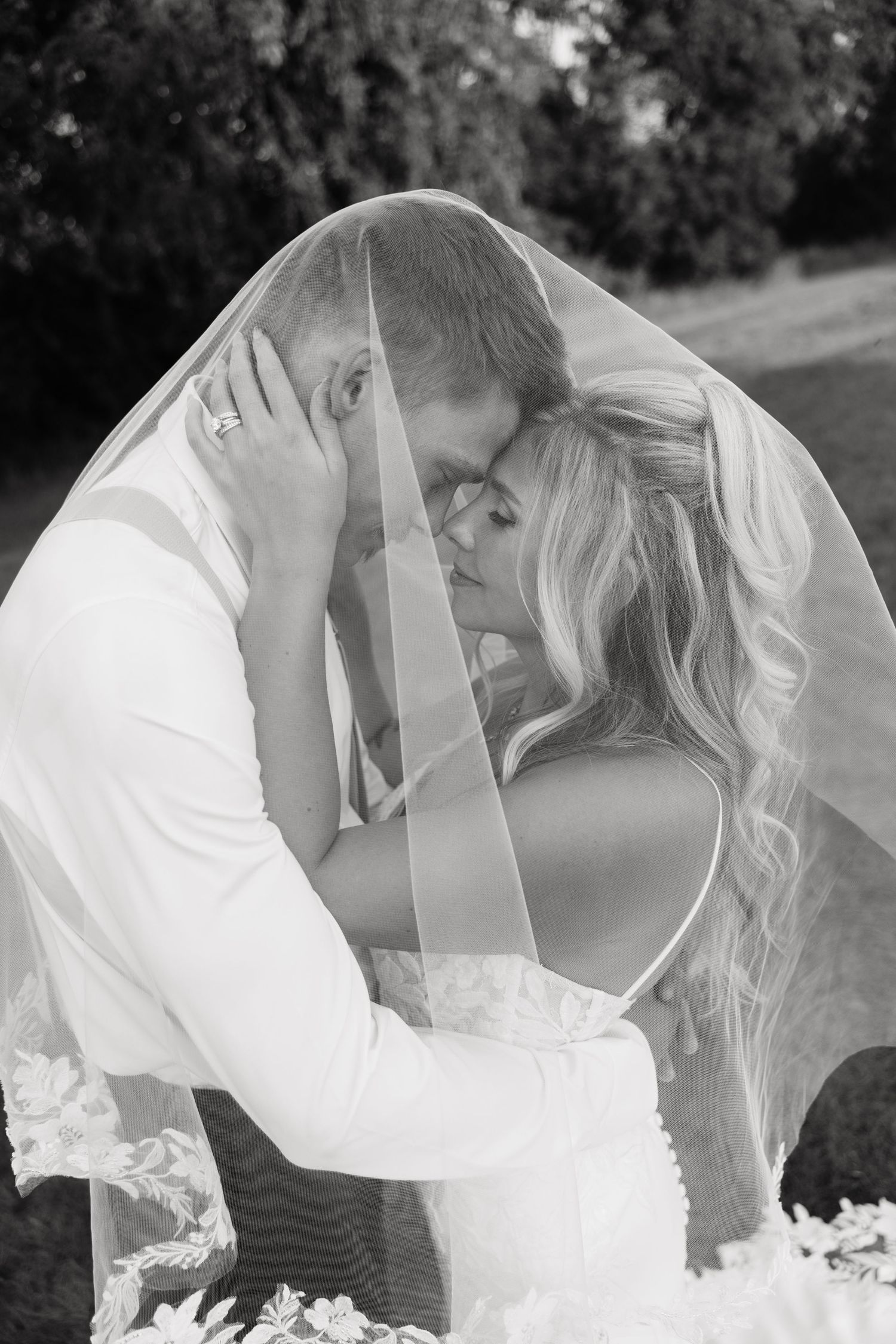 Black and white romantic portrait of bride and groom sharing an intimate moment under a flowing wedding veil.
