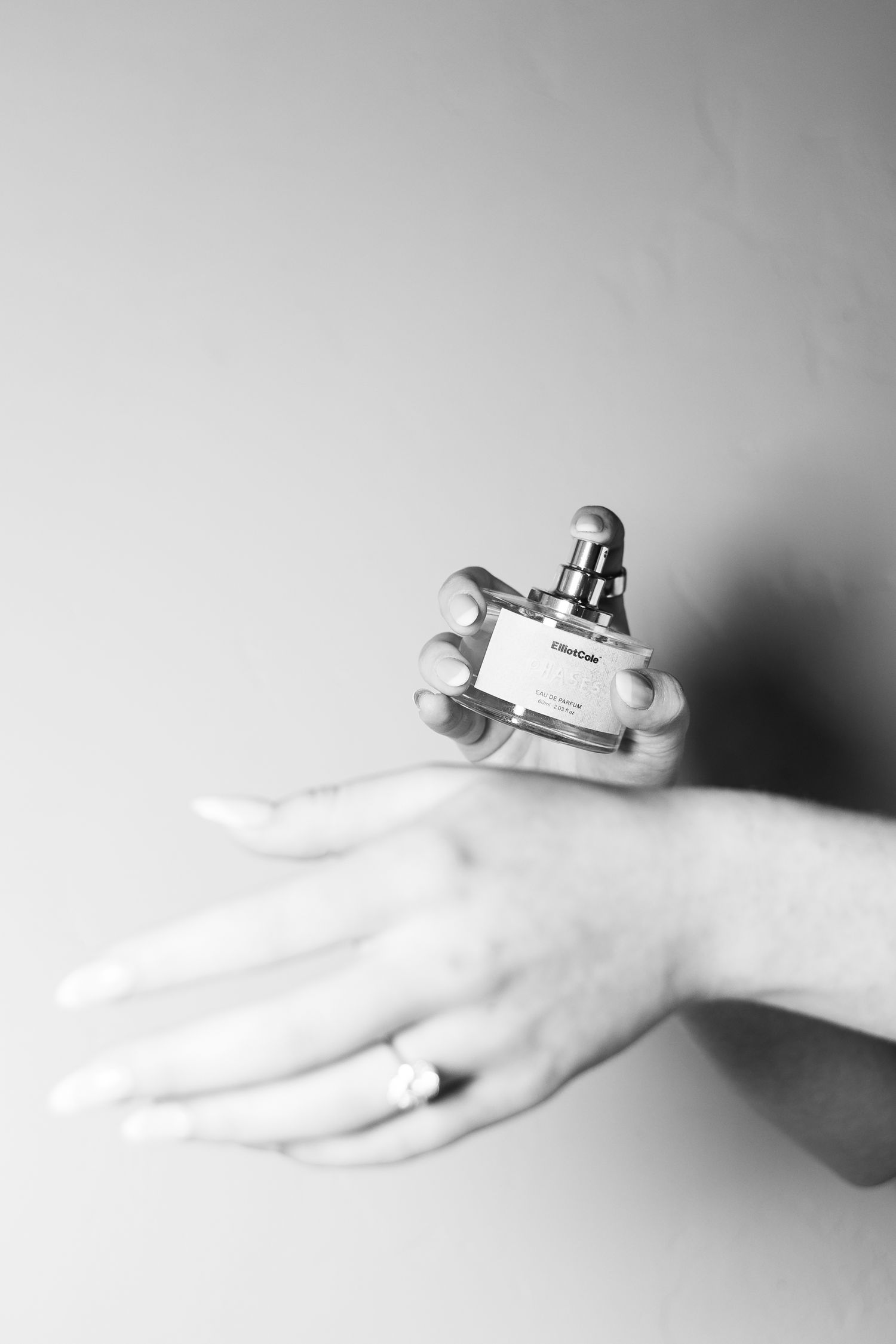 Black and white photo of hands holding a small perfume bottle, one hand wearing a diamond ring.