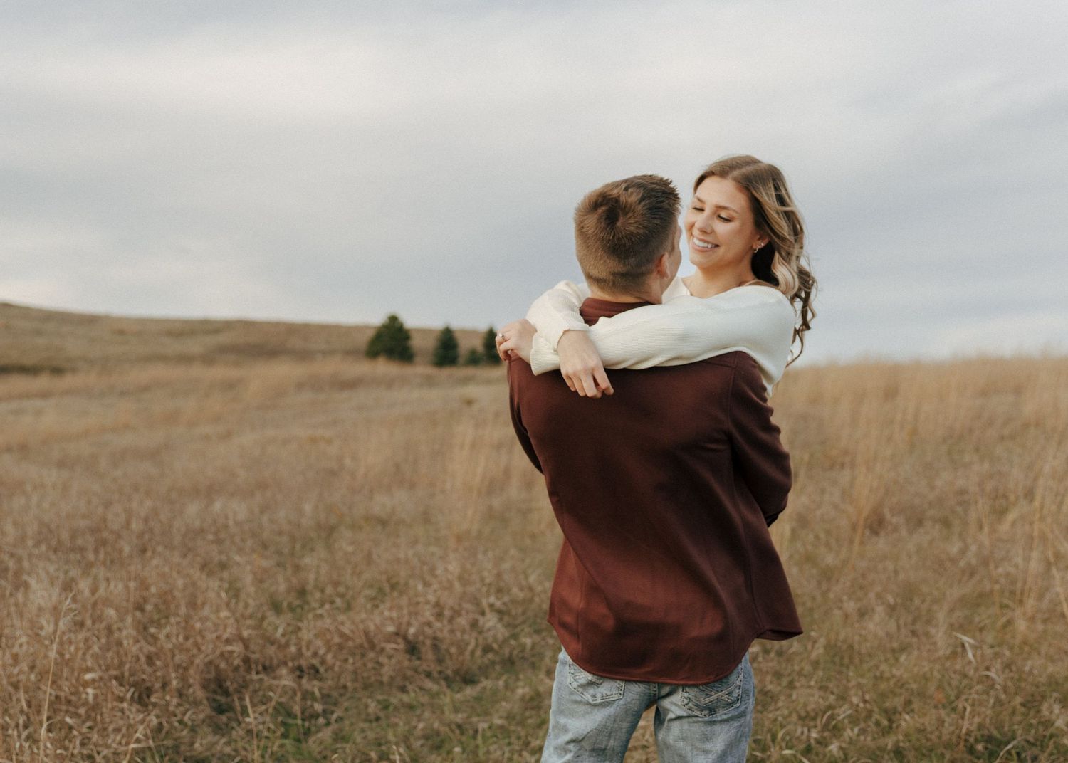 Couple sharing a joyful embrace in an autumn field under cloudy skies.