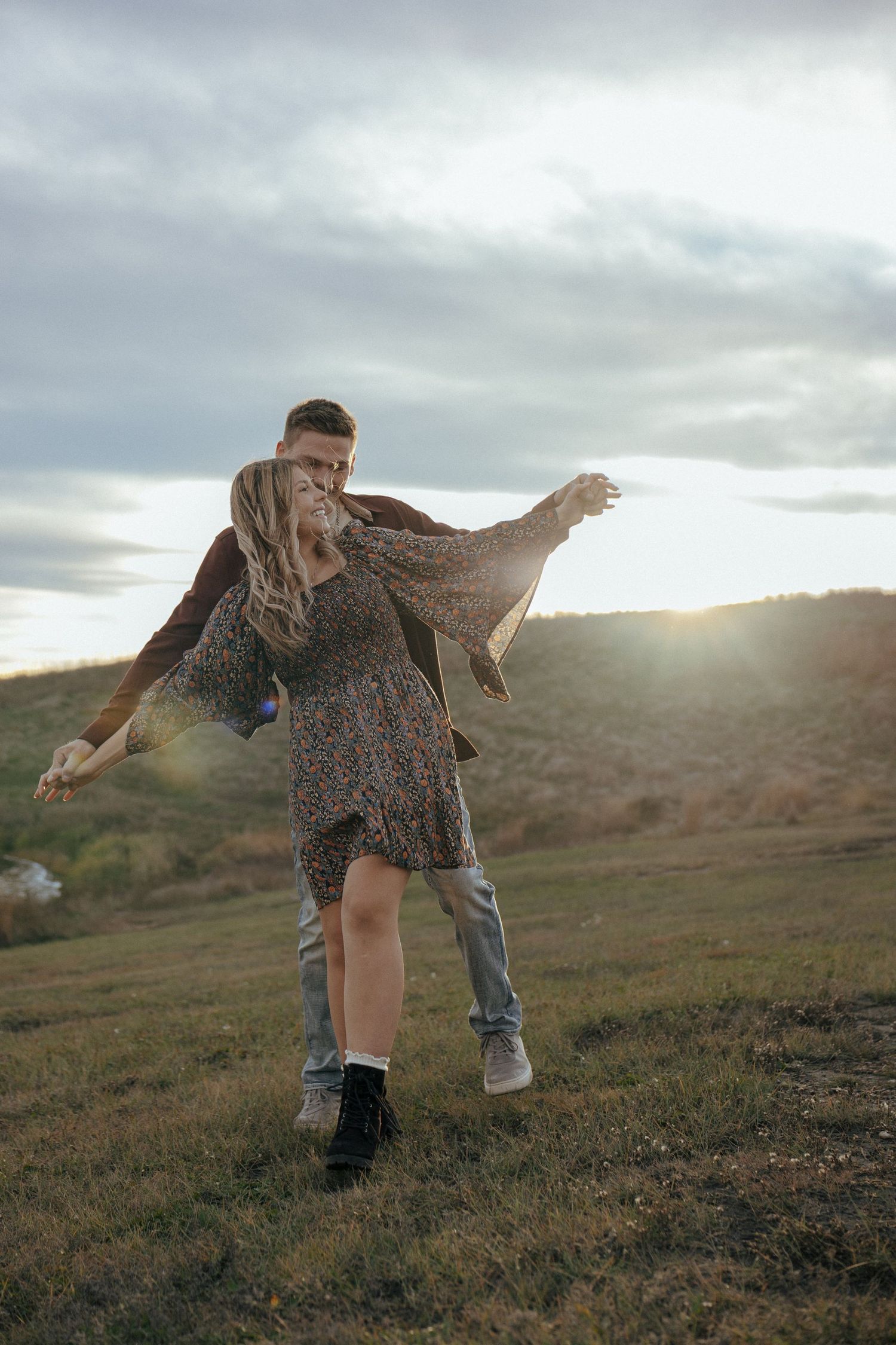 Two people dance and spin together on a hilltop during golden hour.