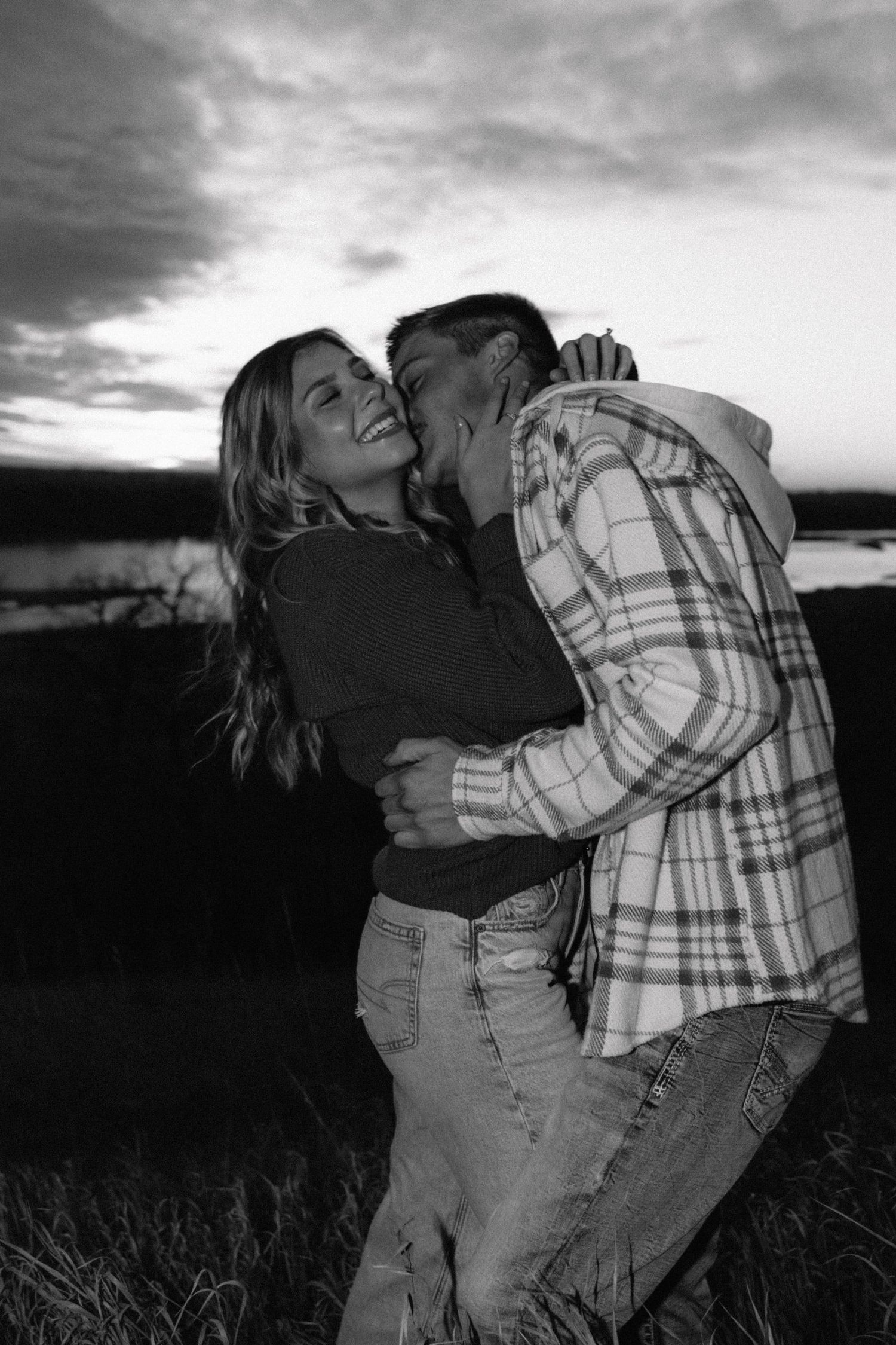 Silhouetted couple in casual wear dancing in a field at twilight.