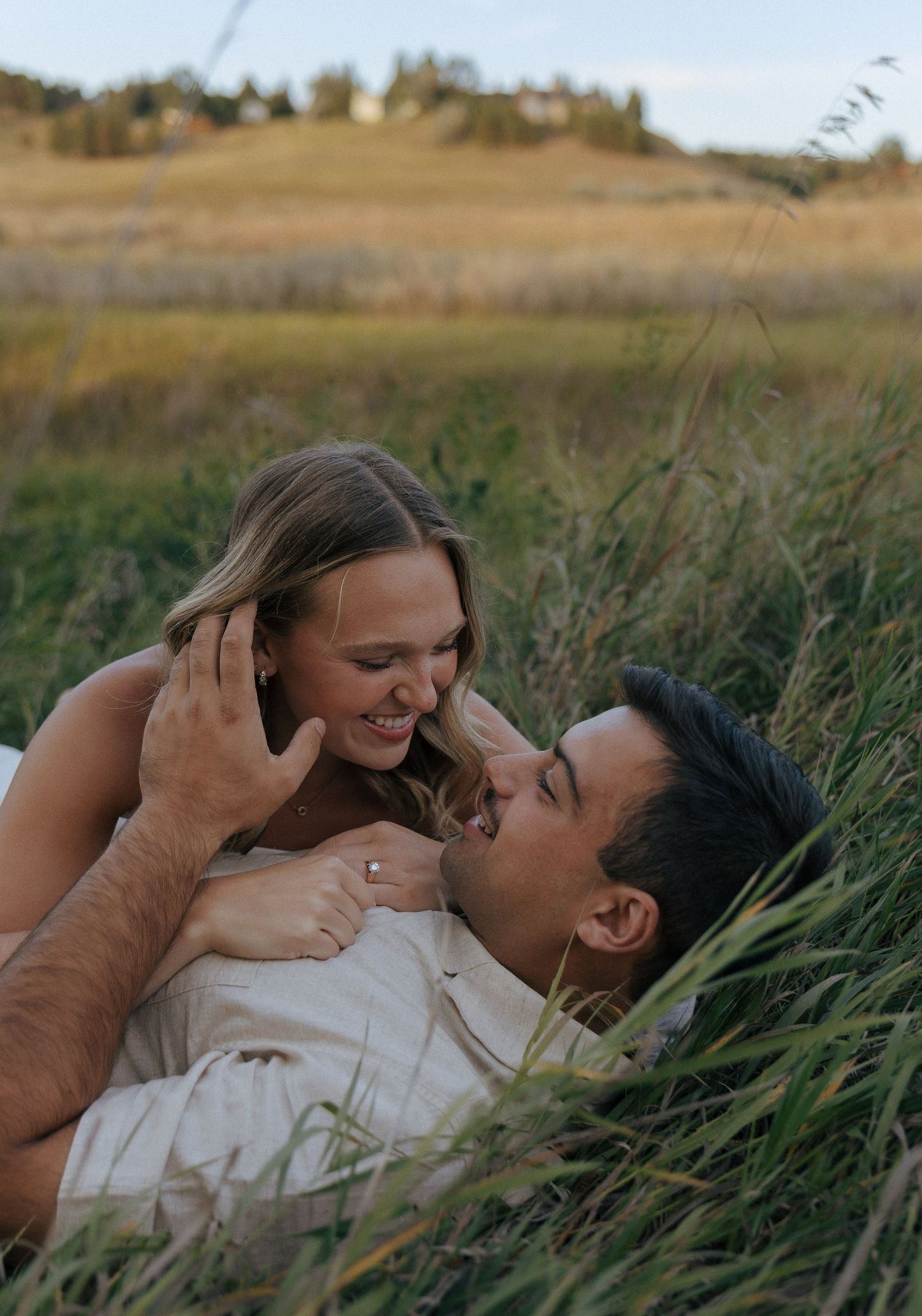 A tender moment between two people lying in tall grass during sunset.