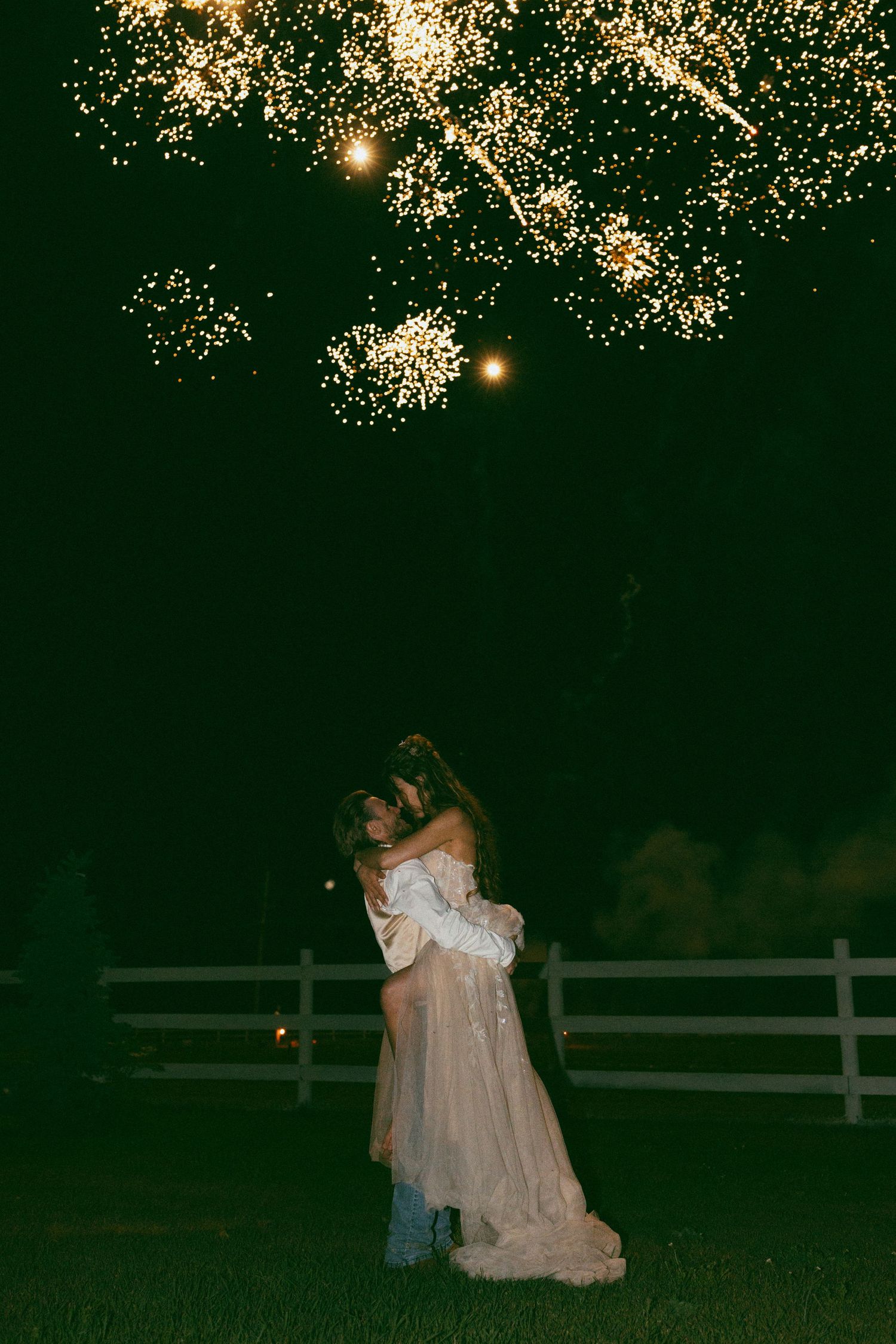 bride and groom kissing as he lifts her up and fireworks are in the background